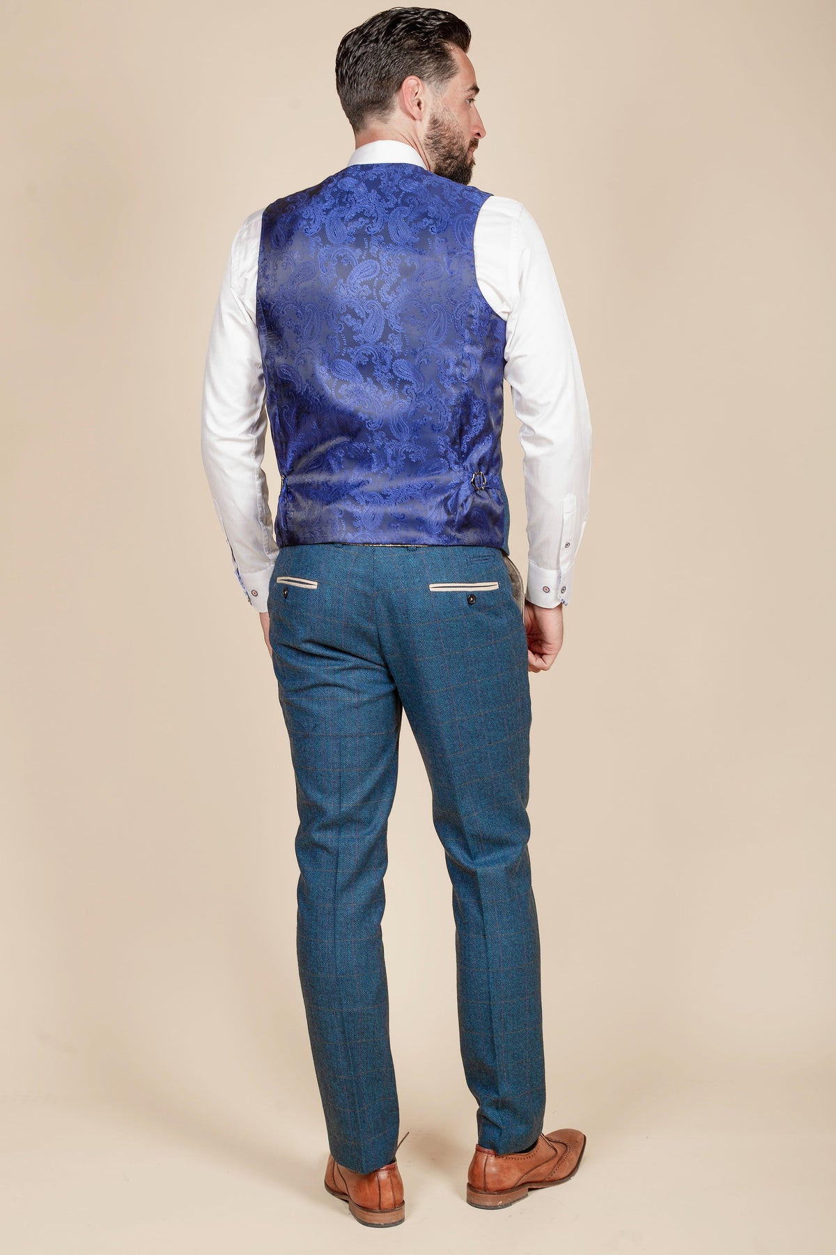 A man stands facing away, wearing the marcdarcy Everton Collection DION Blue Tweed Suit with Kelvin Waistcoat Team Suit against a plain beige background.