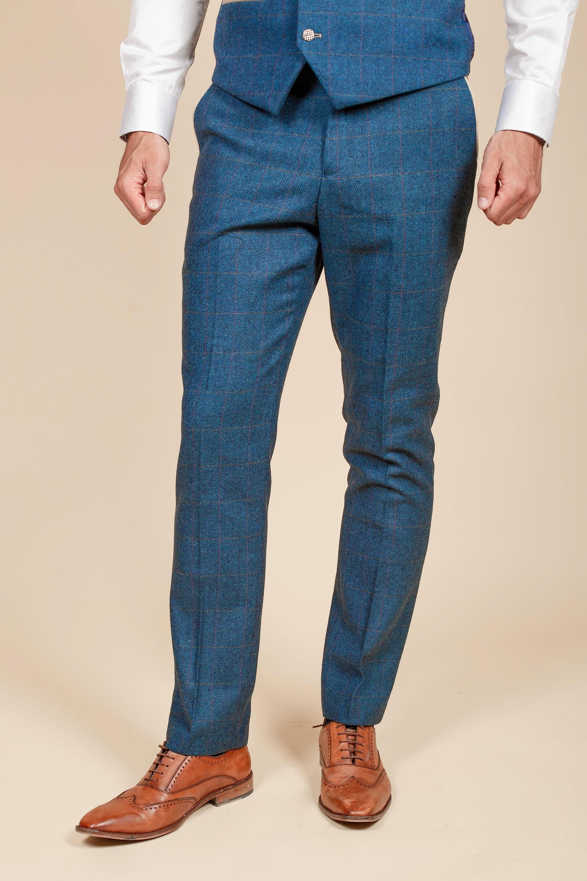 A person dressed in marcdarcys The Everton Collection | Séamus Coleman In DION Blue Tweed Check Suit stands against a beige background; only the blue plaid pants, matching vest, white shirt, and brown leather shoes are visible. Upper body and face are not shown.