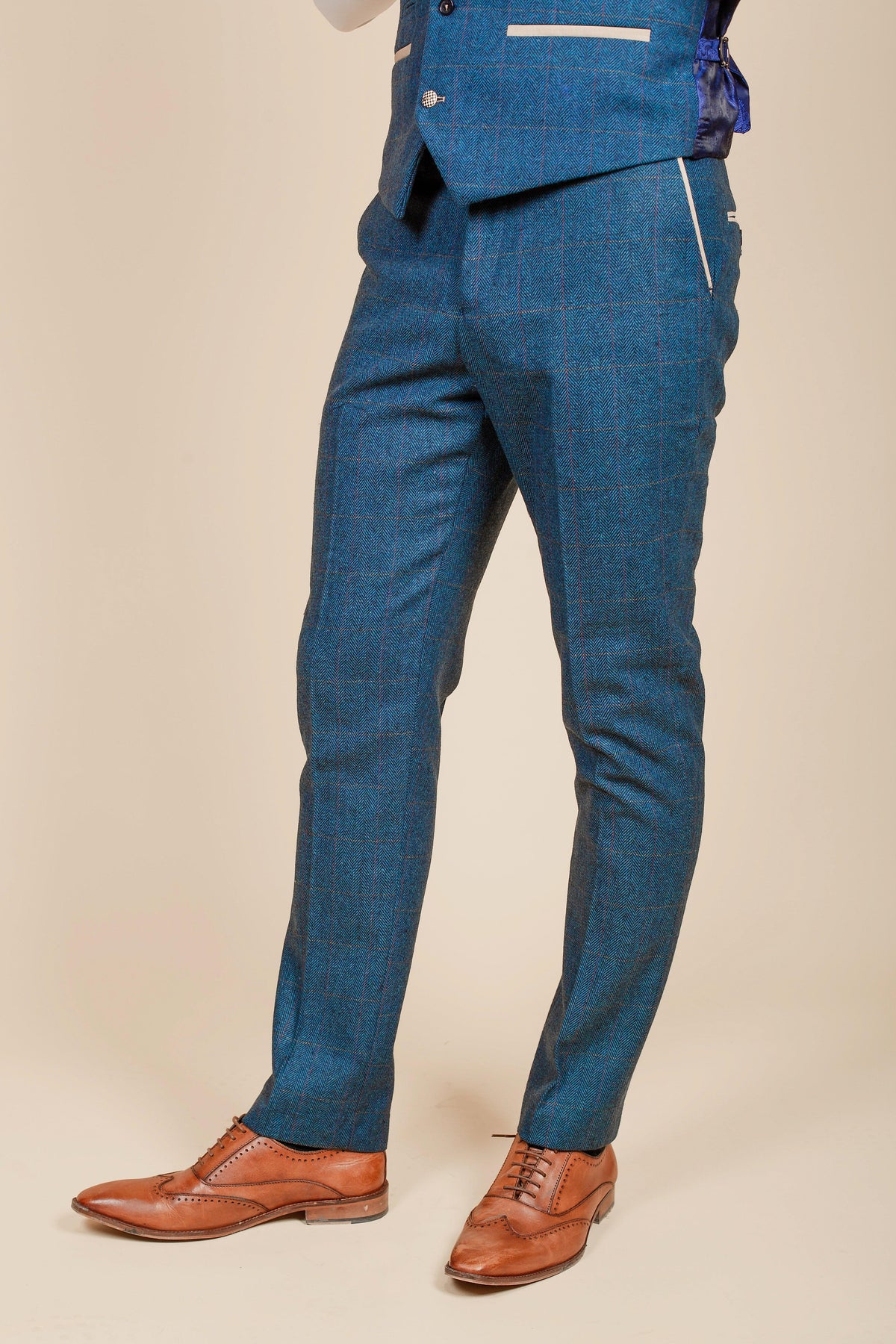 A man's legs are shown wearing the marcdarcy WHU Collection - DION Blue Tweed Check Suit as worn by Crysencio Summerville with brown wingtip shoes, set against a cream background.