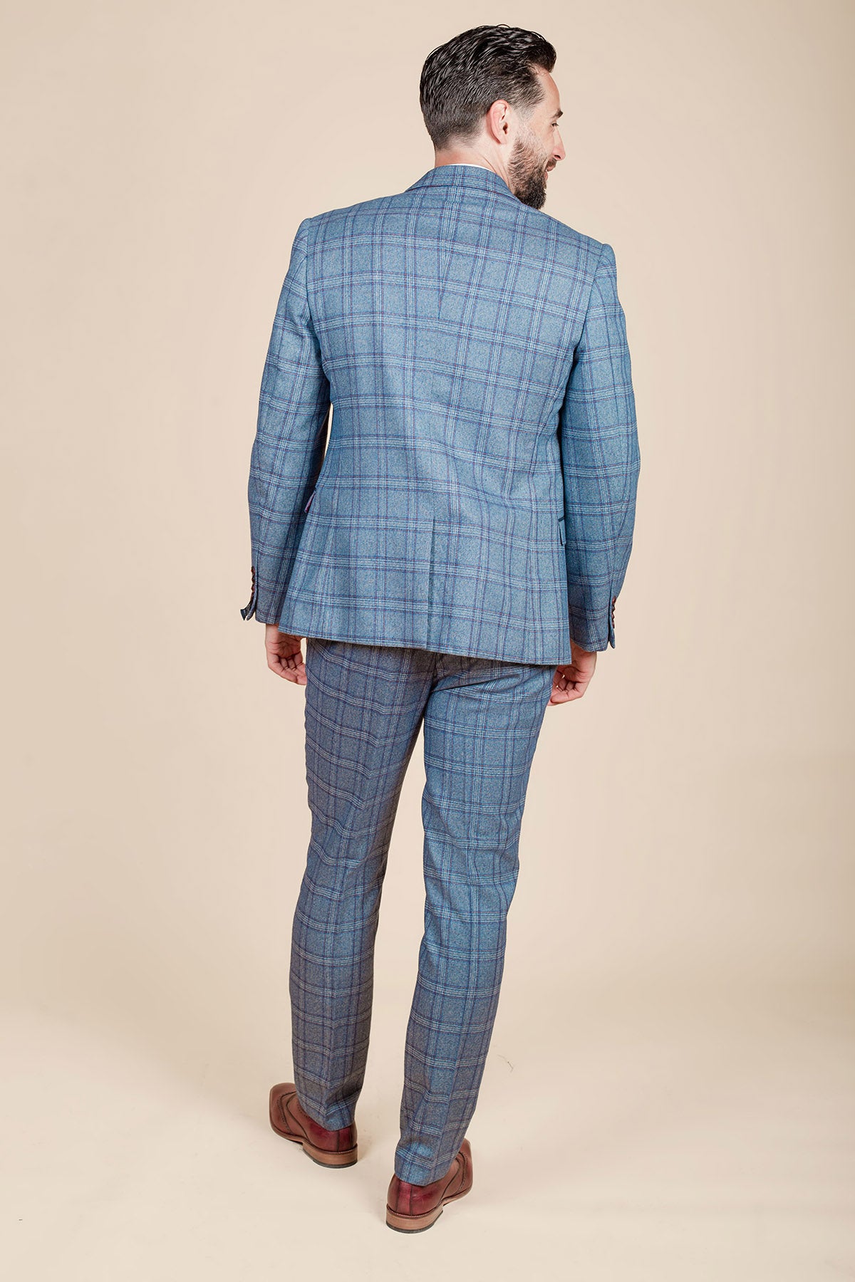 A man faces away, wearing the marcdarcy ABBOTT Blue Tweed Check Blazer with brown shoes, showcasing a blend of contemporary heritage style against a plain beige backdrop.