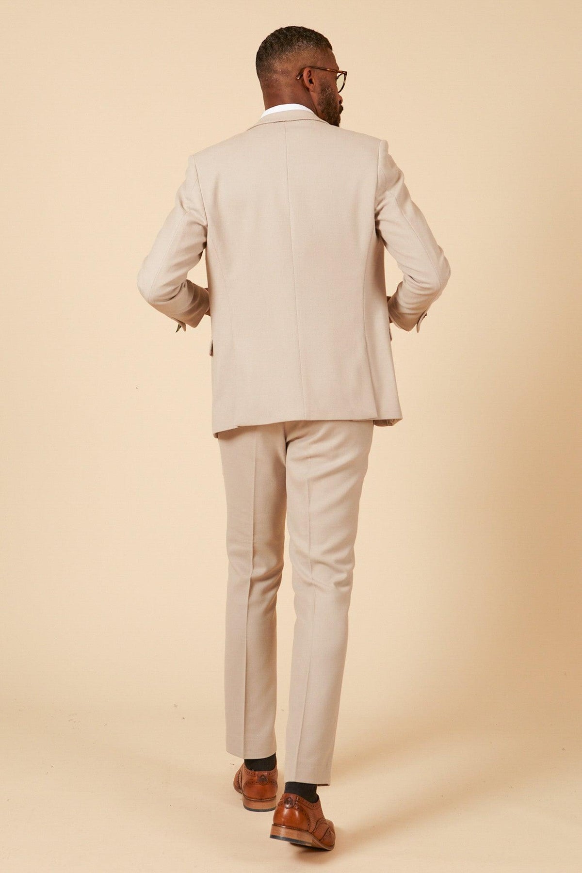 A man in the Marc Darcy Leicester City F.C. Collection HM5 Stone Suit with Kelvin Black Waistcoat, as worn by Mads Hermansen, stands facing away from the camera against a plain beige background.