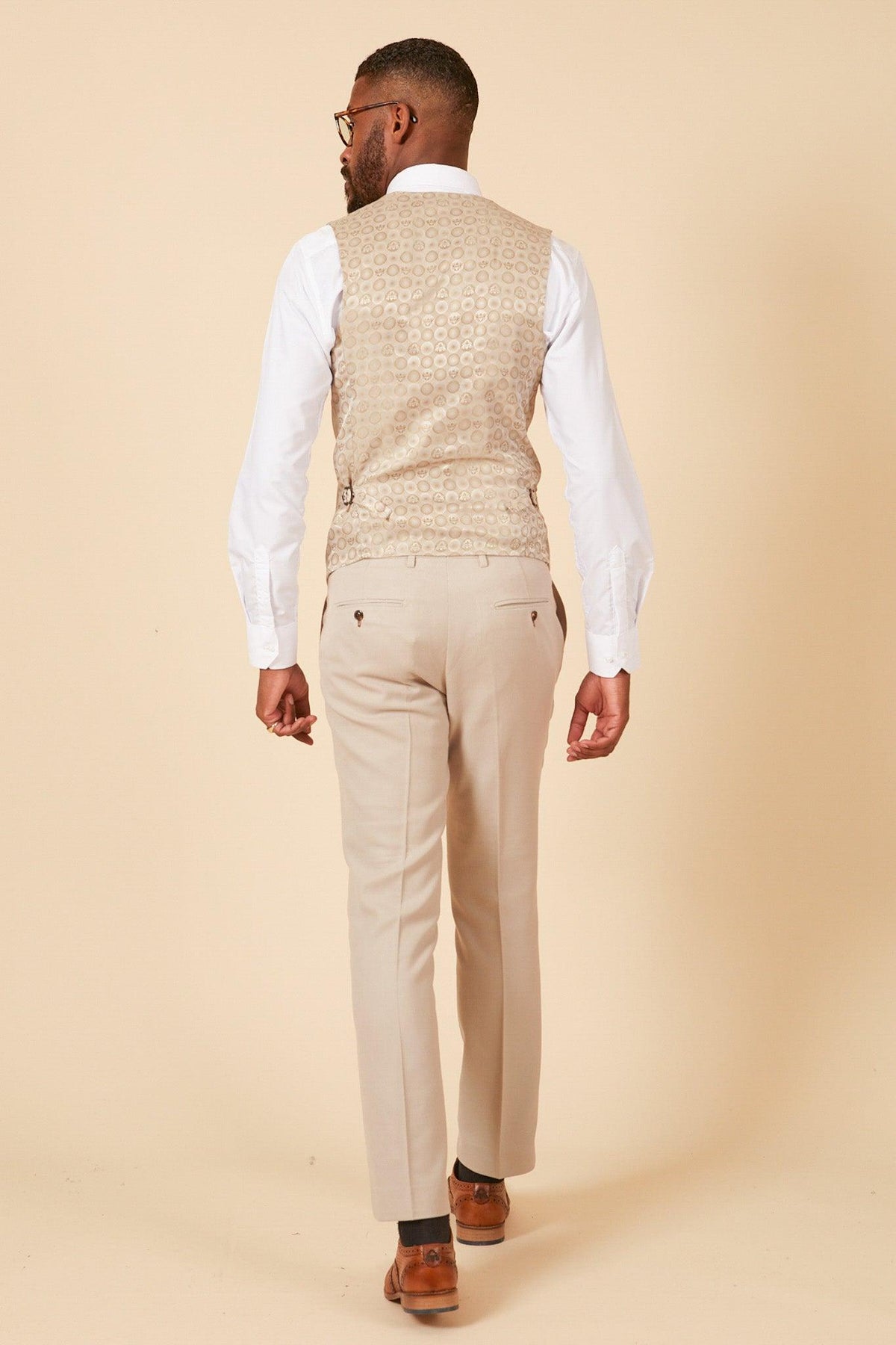 A man stands facing away in the Marc Darcy Leicester City F.C. Collection HM5 Stone Suit with Kelvin Black Waistcoat, as worn by Mads Hermansen, against a plain beige background.