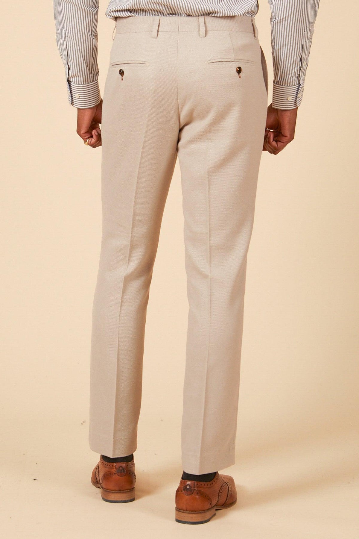 A person faces away, wearing the Marc Darcy Leicester City F.C. Collection HM5 Stone Suit with Kelvin Black Waistcoat as worn by Mads Hermansen. The slim-fit beige pants have buttoned back pockets; the background is light beige.