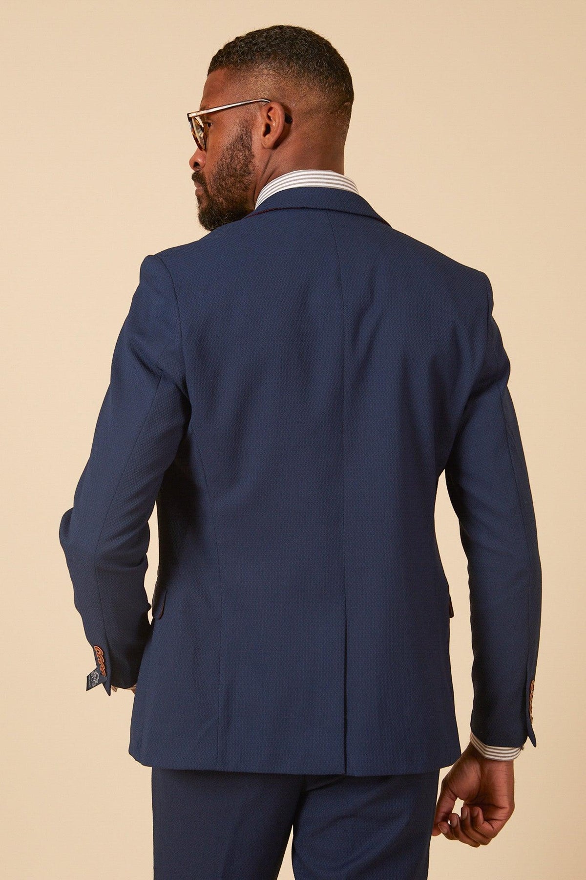 Rear view of a man in marcdarcy's The Leicester City F.C. Collection - MAX Royal Blue Suit as worn by Wilfred Ndidi, paired with a striped shirt. He has glasses and a beard.