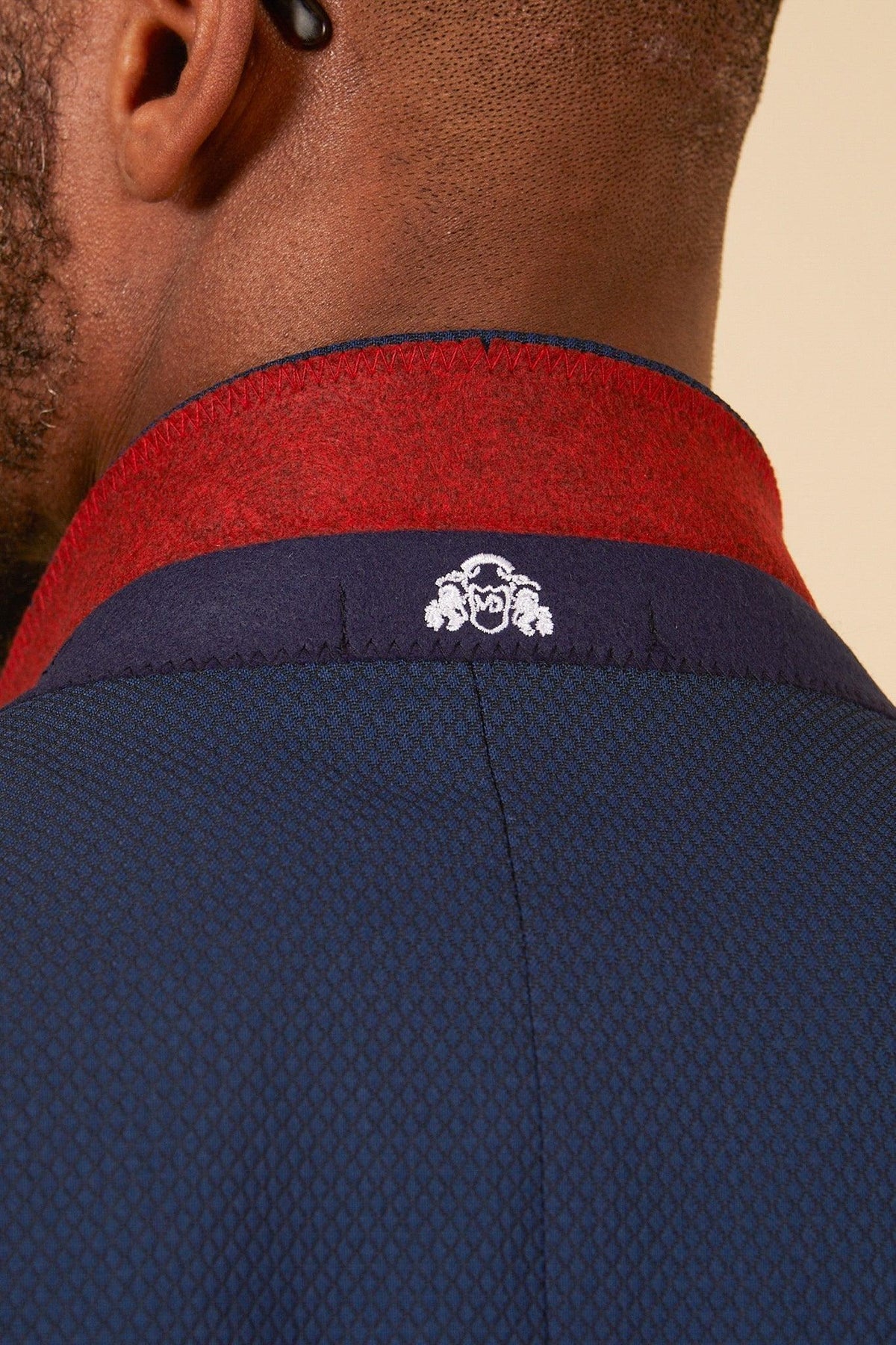 Close-up of a person’s neck wearing the marcdarcy Leicester City F.C. Collection - MAX Royal Blue Suit, as worn by Harry Winks, featuring a red and navy collar with a white embroidered logo at the center for refined club style.