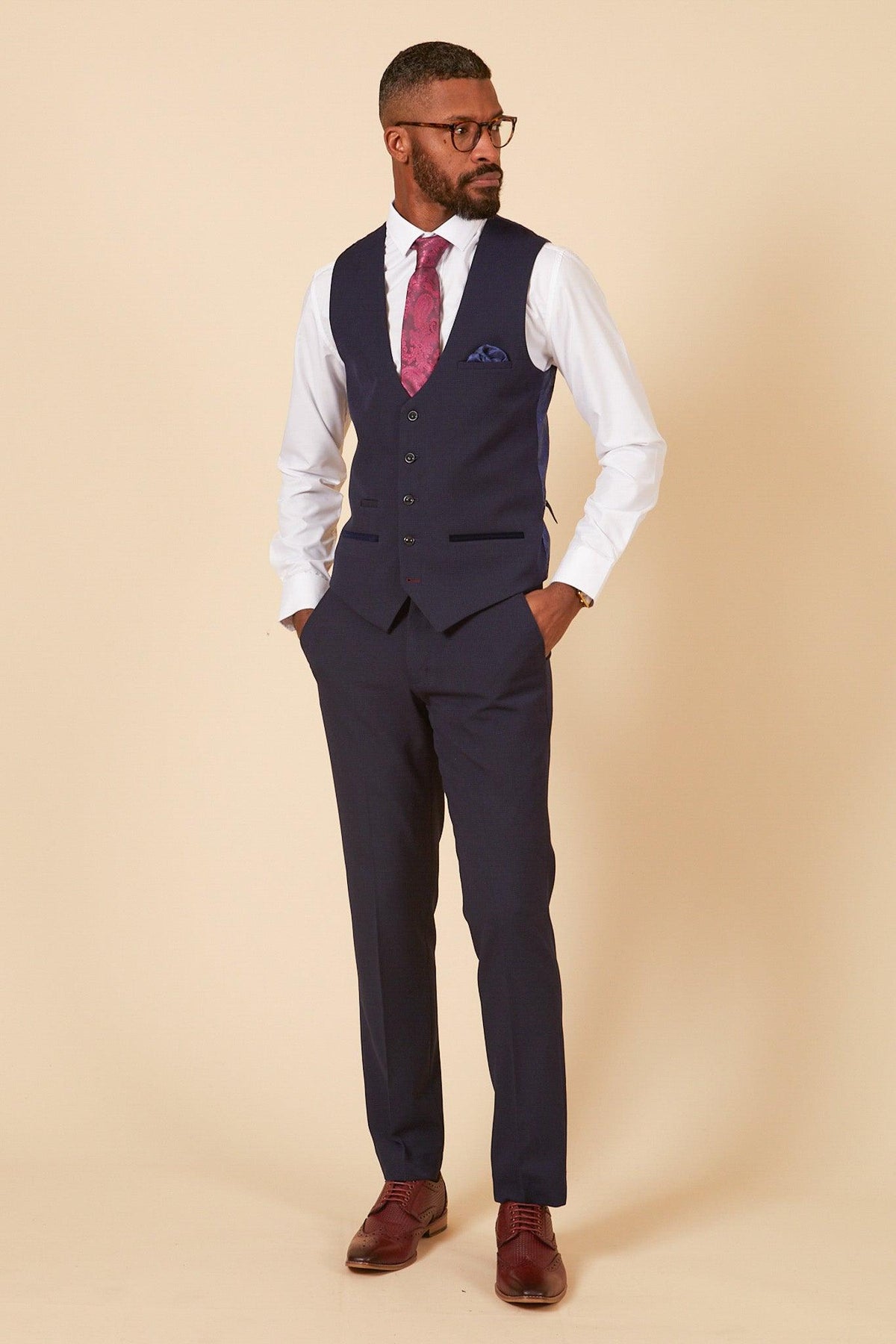 West Ham United footballer Jarrod Bowen wears a Marc Darcy Bromley navy check suit, white shirt, patterned tie, and glasses, standing with hands in pockets against a cream background.