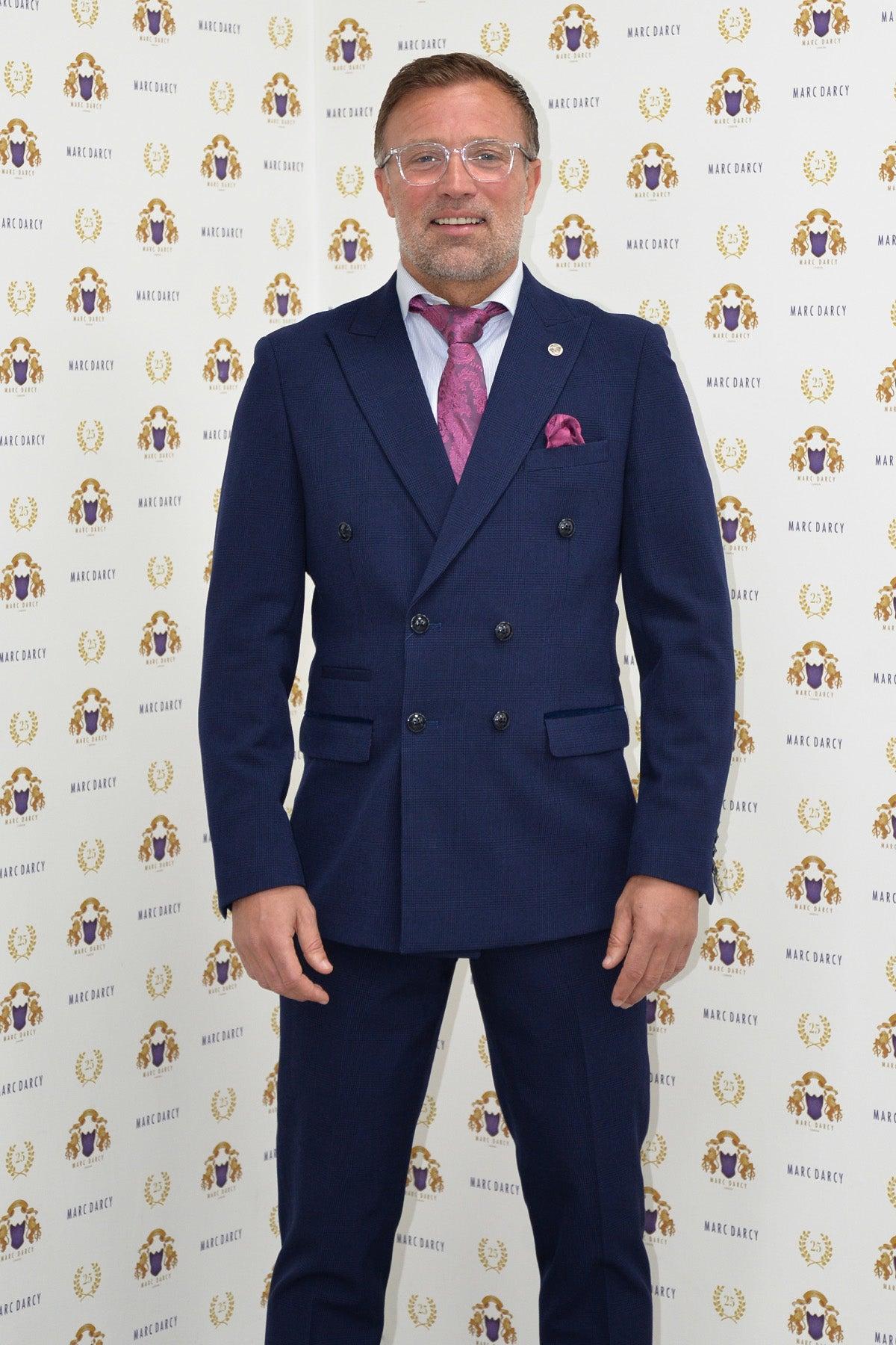 Former Sunderland footballer Michael Gray wears a Bromley Navy Double-Breasted Suit by Marc Darcy, standing in front of a step-and-repeat backdrop with gold and purple Marc Darcy logos.