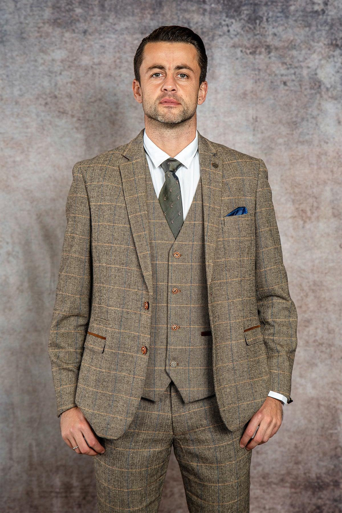 A man wearing marcdarcy's WHU Collection TED Tan Tweed Check Three Piece Suit, as worn by Lukasz Fabianski, poses confidently before a mottled brown and gray background.
