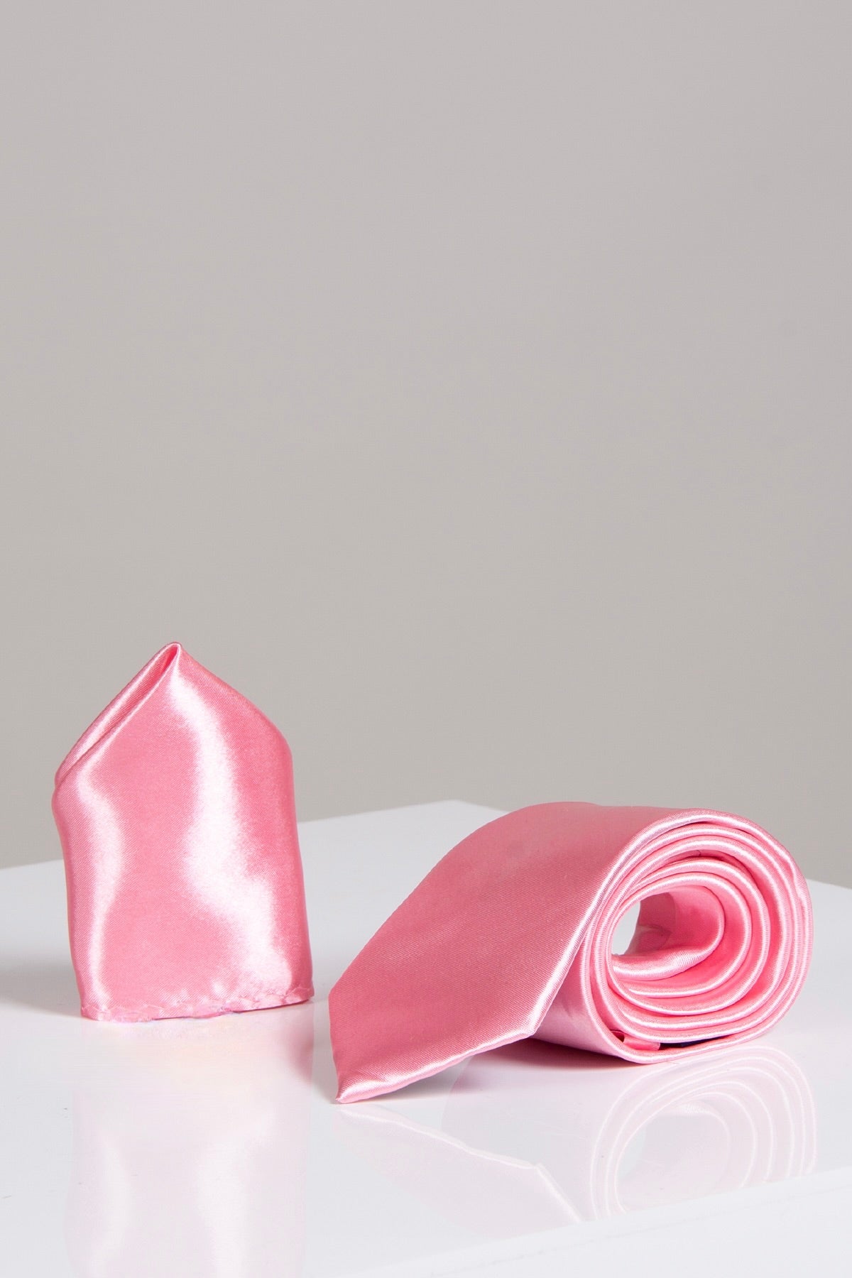 The Accessory ST - Satin Tie and Pocket Square Set in Blush Pink showcases a satin tie rolled beside a matching pocket square, elegantly displayed on a white surface with a light gray background.