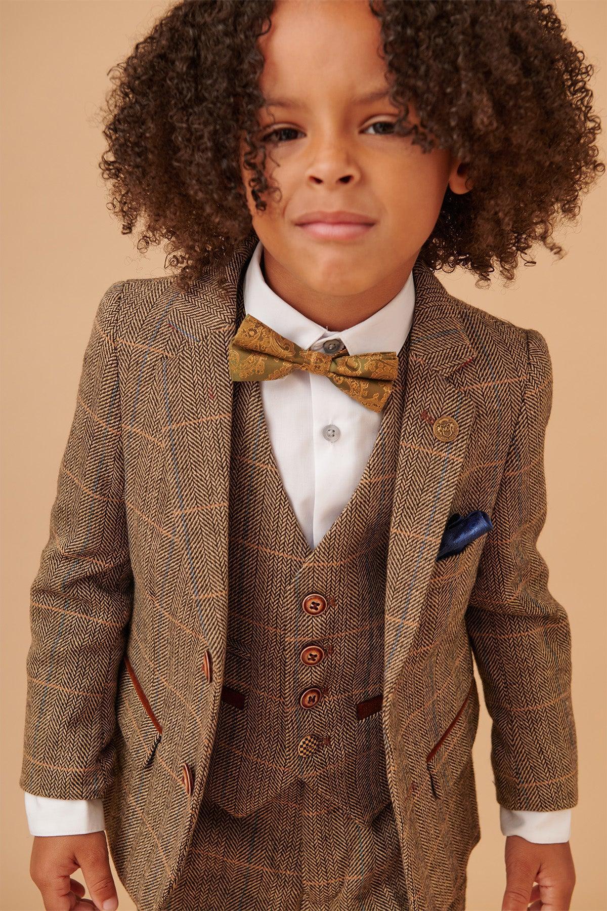 A young child wears the marcdarcy TED Children's Tan Tweed Check Three Piece Suit, styled with a patterned bow tie and blue pocket square, standing against a beige background and looking confidently at the camera.