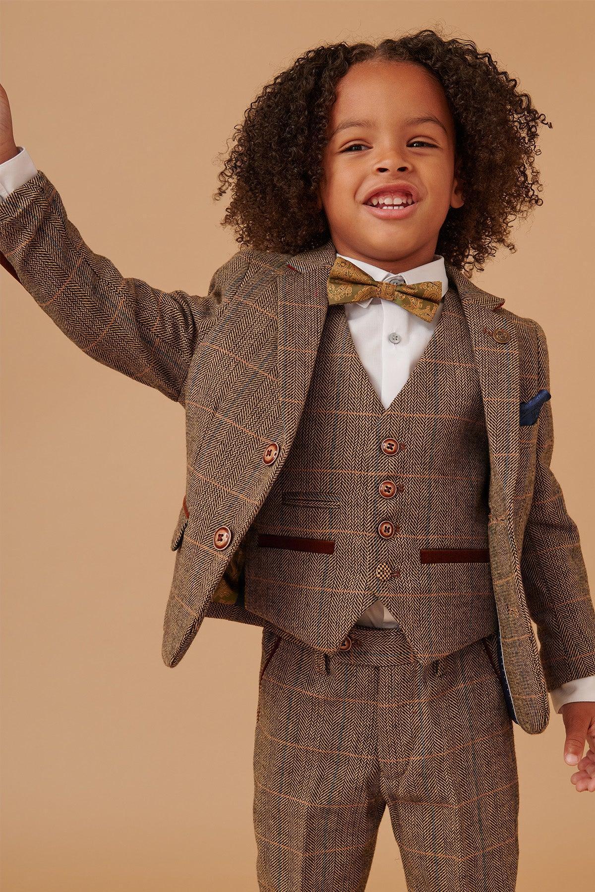 A young Black boy with curly hair smiles in the marcdarcy TED Children's Tan Tweed Check Three Piece Suit, featuring a vintage look with orange plaid accents, styled with a white shirt and gold paisley bow tie—ideal for a country wedding.