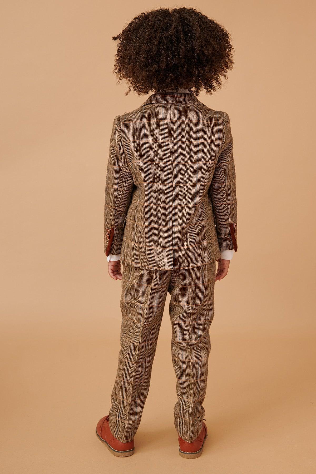 A child with curly hair, seen from behind, wears the marcdarcy TED Childrens Tan Tweed Check Three Piece Suit and brown shoes, standing against a beige background.