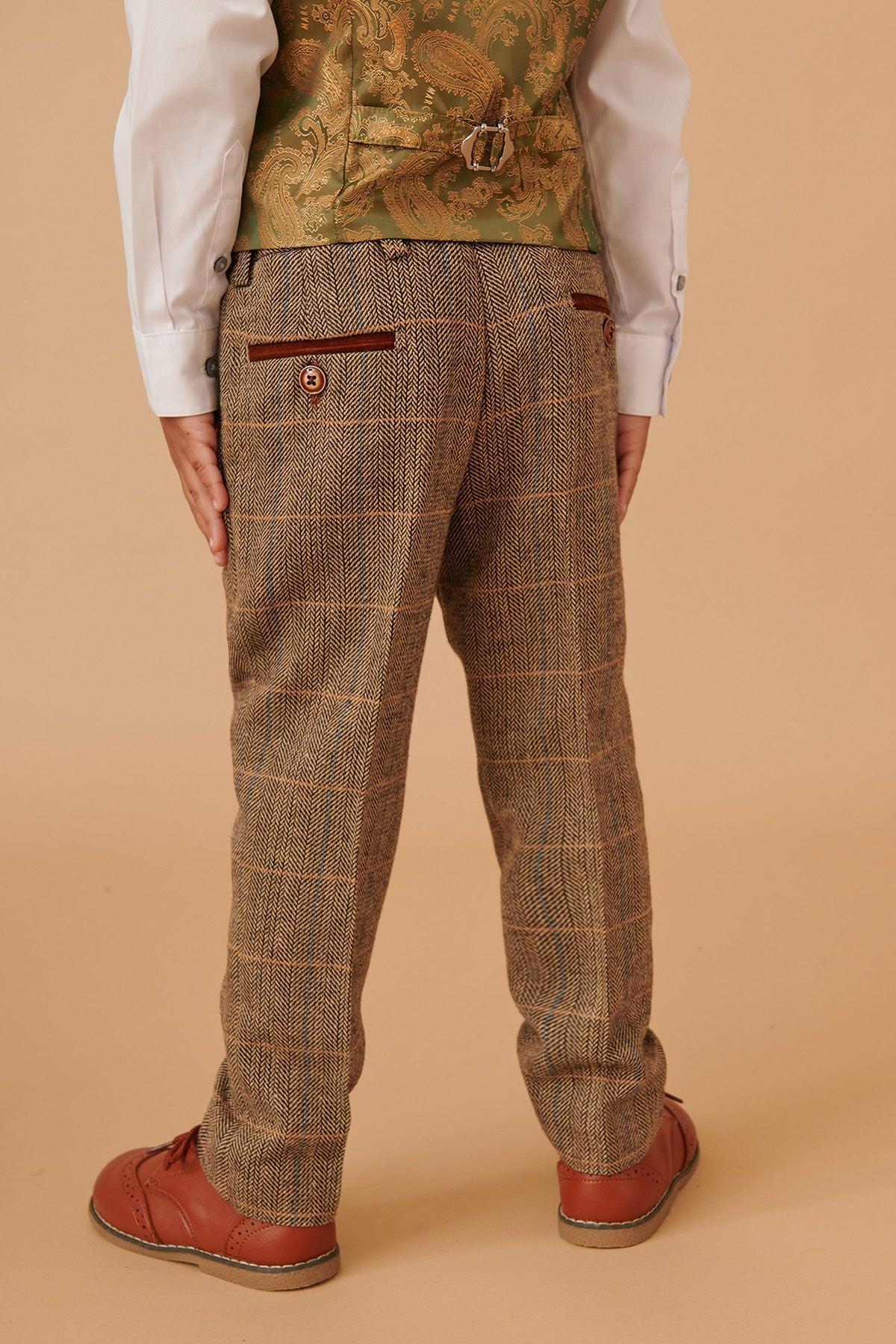 A child faces away, dressed in the marcdarcy TED Childrens Tan Tweed Check Three Piece Suit, featuring vintage-inspired plaid trousers, a matching vest, and a white shirt with brown shoes against a beige background.