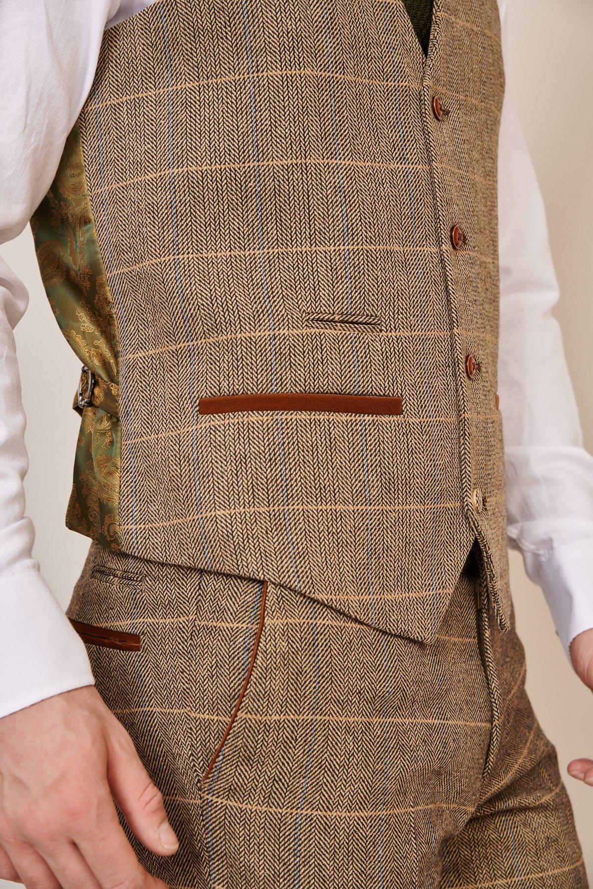A man wears the marcdarcy WHU Collection TED Tan Tweed Check Three Piece Suit, as worn by Lukasz Fabianski, featuring a brown plaid vest over a white shirt and matching plaid trousers.