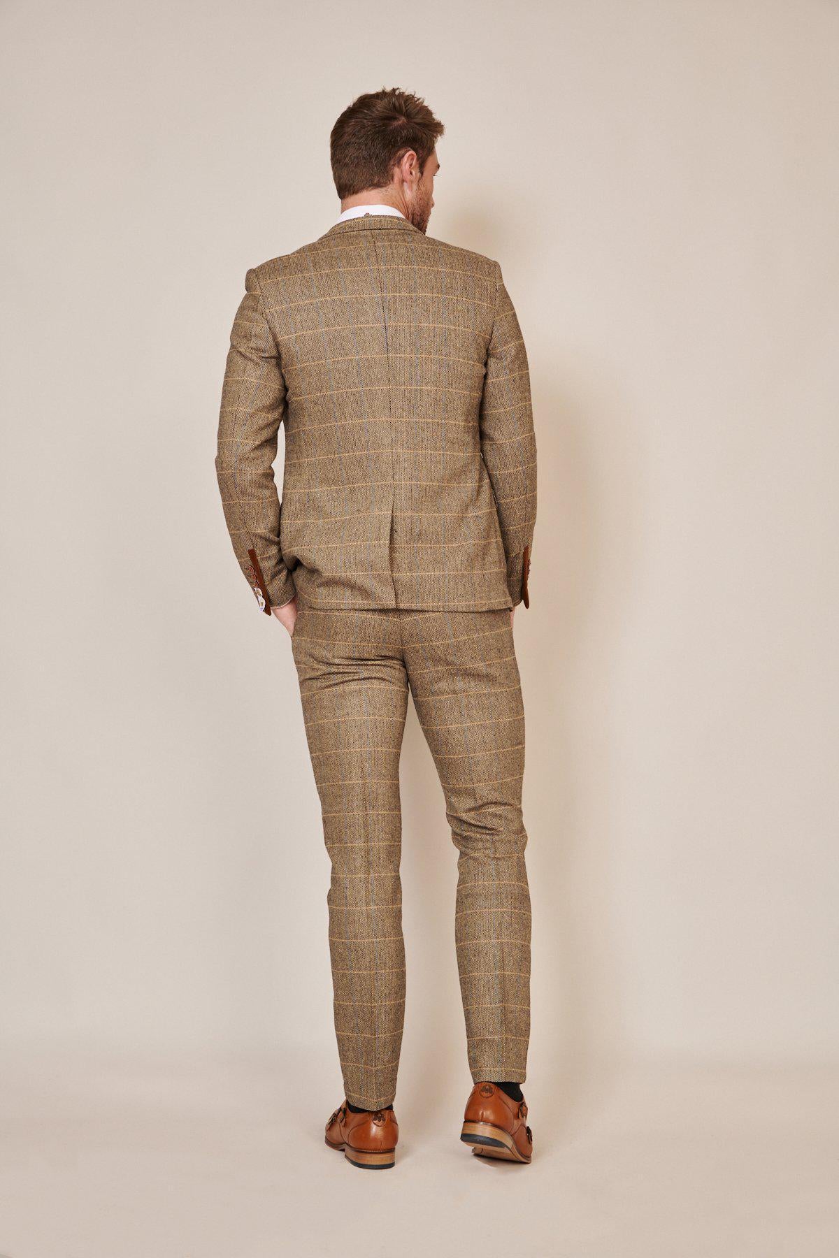 A man stands with his back to the camera, dressed in marcdarcy’s The WHU Collection - TED Tan Tweed Check Three Piece Suit as worn by Lukasz Fabianski, set against a plain beige background.