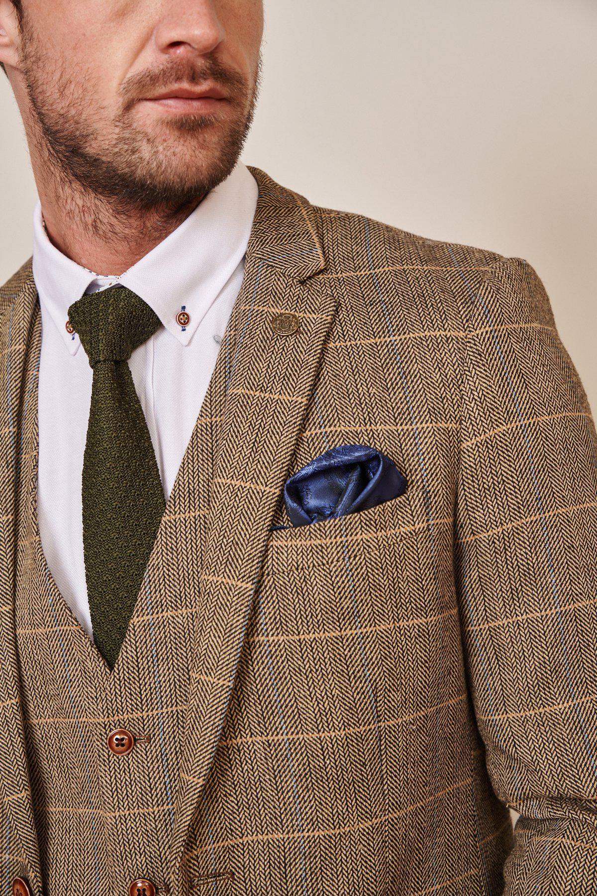 Close-up of a man in the marcdarcy WHU Collection - TED Tan Tweed Suit with Dion Waistcoat as worn by Lukasz Fabianski, styled with a white shirt, green tie, and blue pocket square.