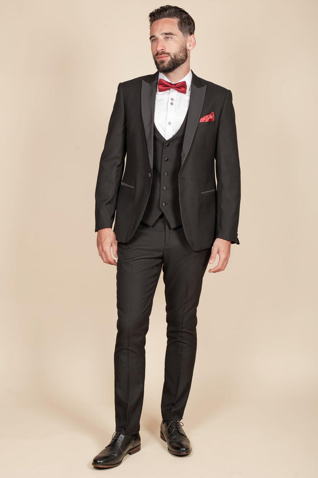 Coronation Street’s Dylan Wilson (Liam McCheyne) wears the marcdarcy Dalton Black Tuxedo Suit—slim fit blazer, white shirt, red bow tie, and brogue shoes—perfect for black tie events against a beige background.