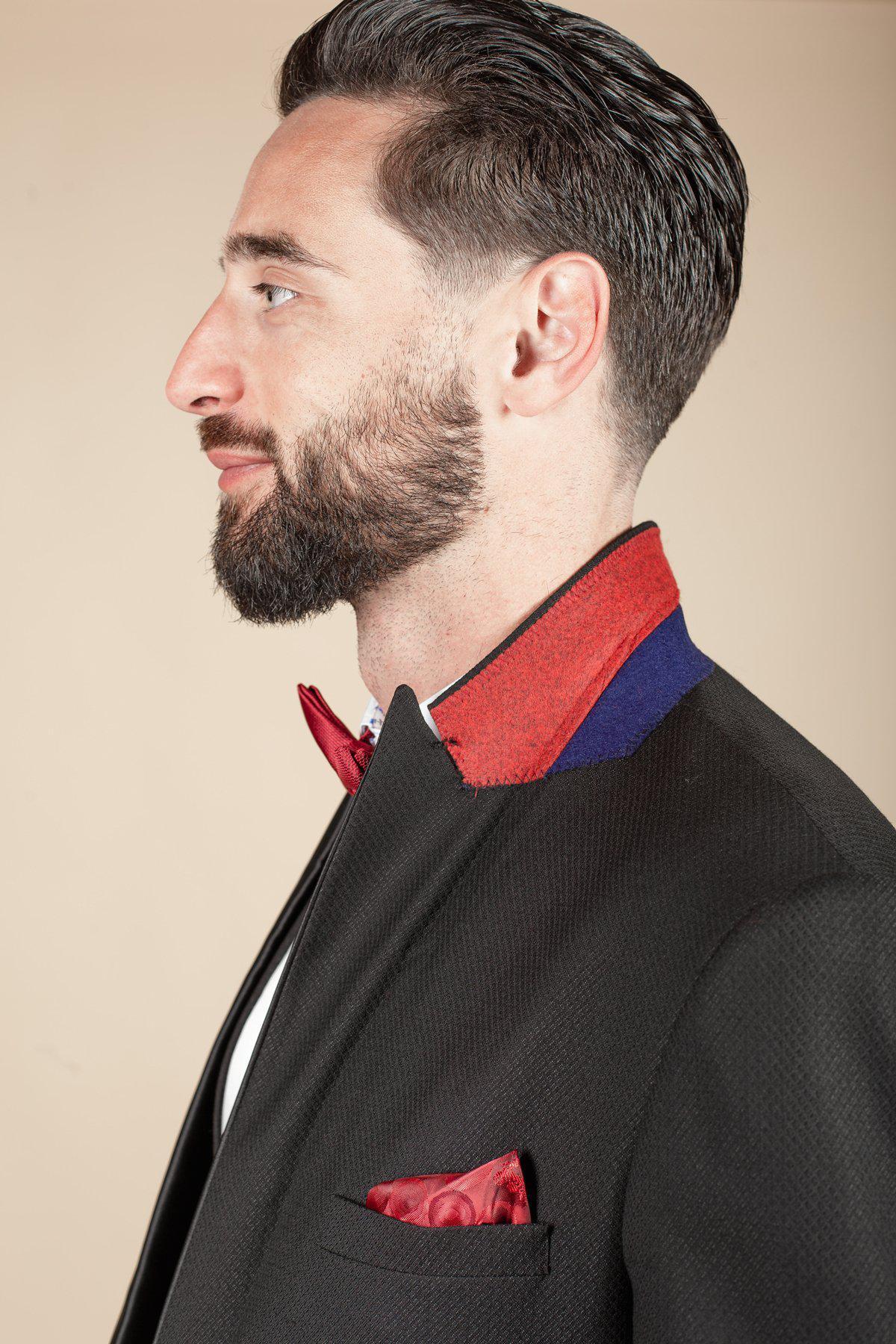 Coronation Streets Dylan Wilson (Liam McCheyne) is shown in profile wearing a marcdarcy Dalton Black Tuxedo Suit with satin peak lapel, red and blue collar, red bow tie, and red pocket square against a beige background.