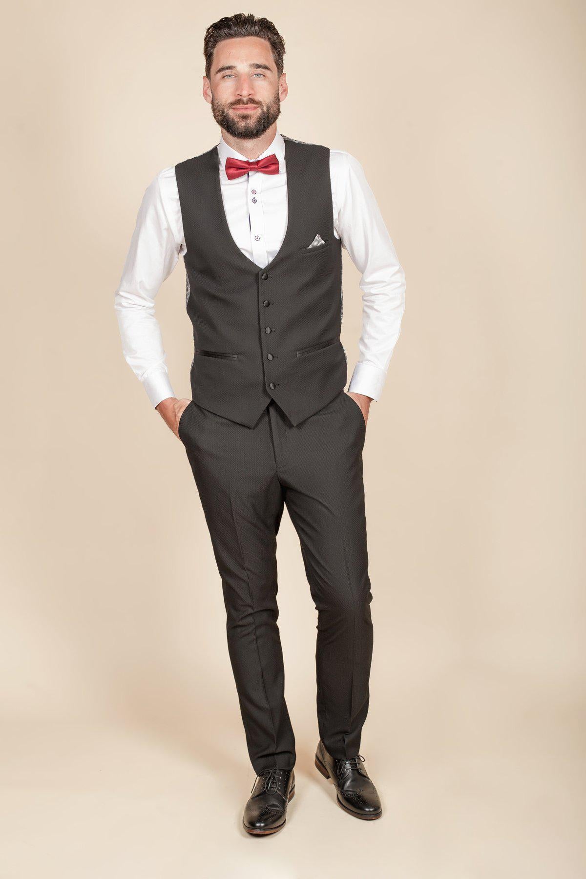 Coronation Street's Dylan Wilson (Liam McCheyne) wears a marcdarcy Dalton Black Tuxedo Suit with a slim fit blazer, white shirt, and red bowtie, standing with his hands in his pockets.