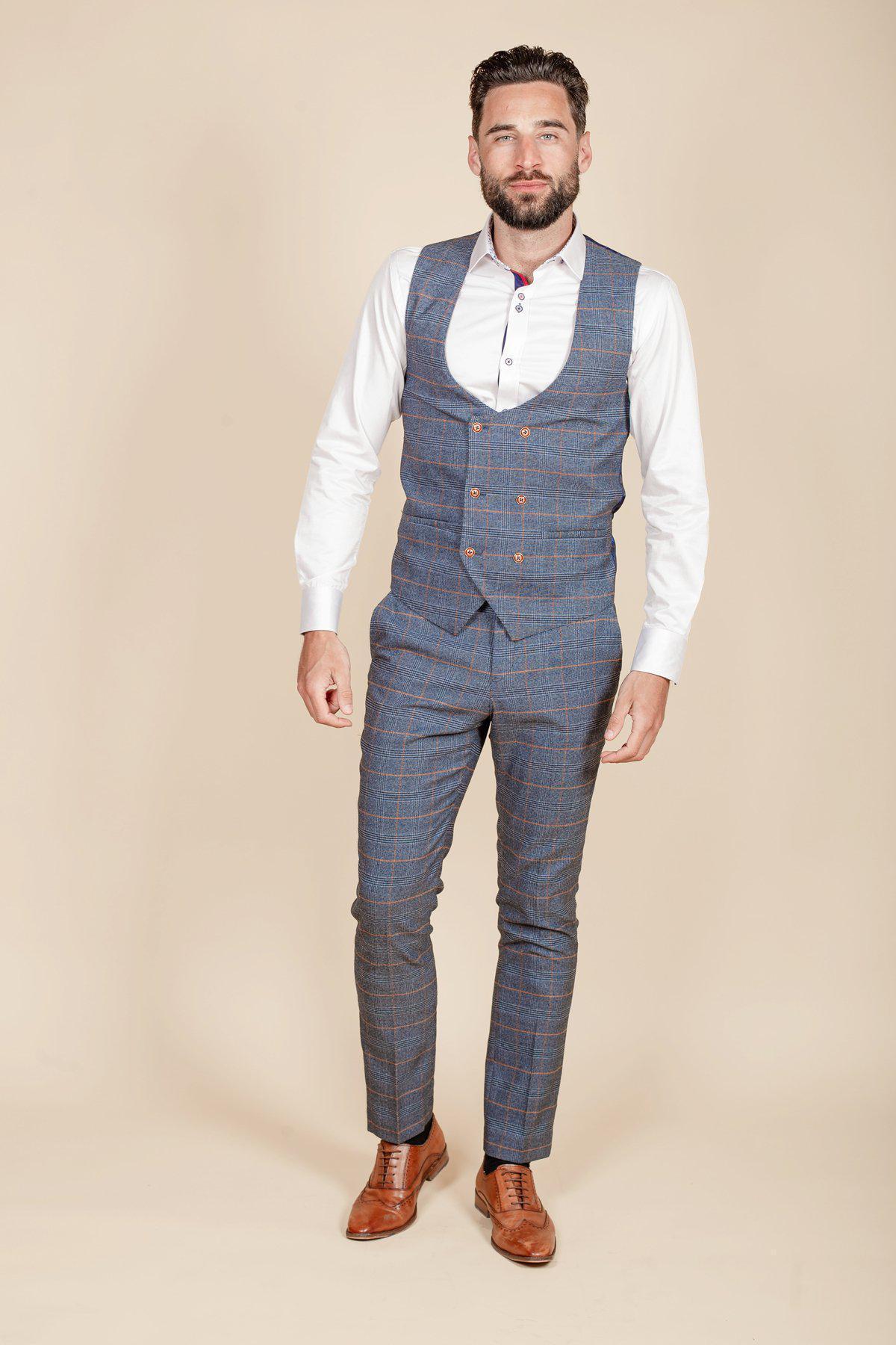Rob Mallard as Daniel Osbourne from Coronation Street wears the marcdarcy JENSON Sky Blue Check Suit with a white shirt and brown dress shoes, standing against a plain beige background.