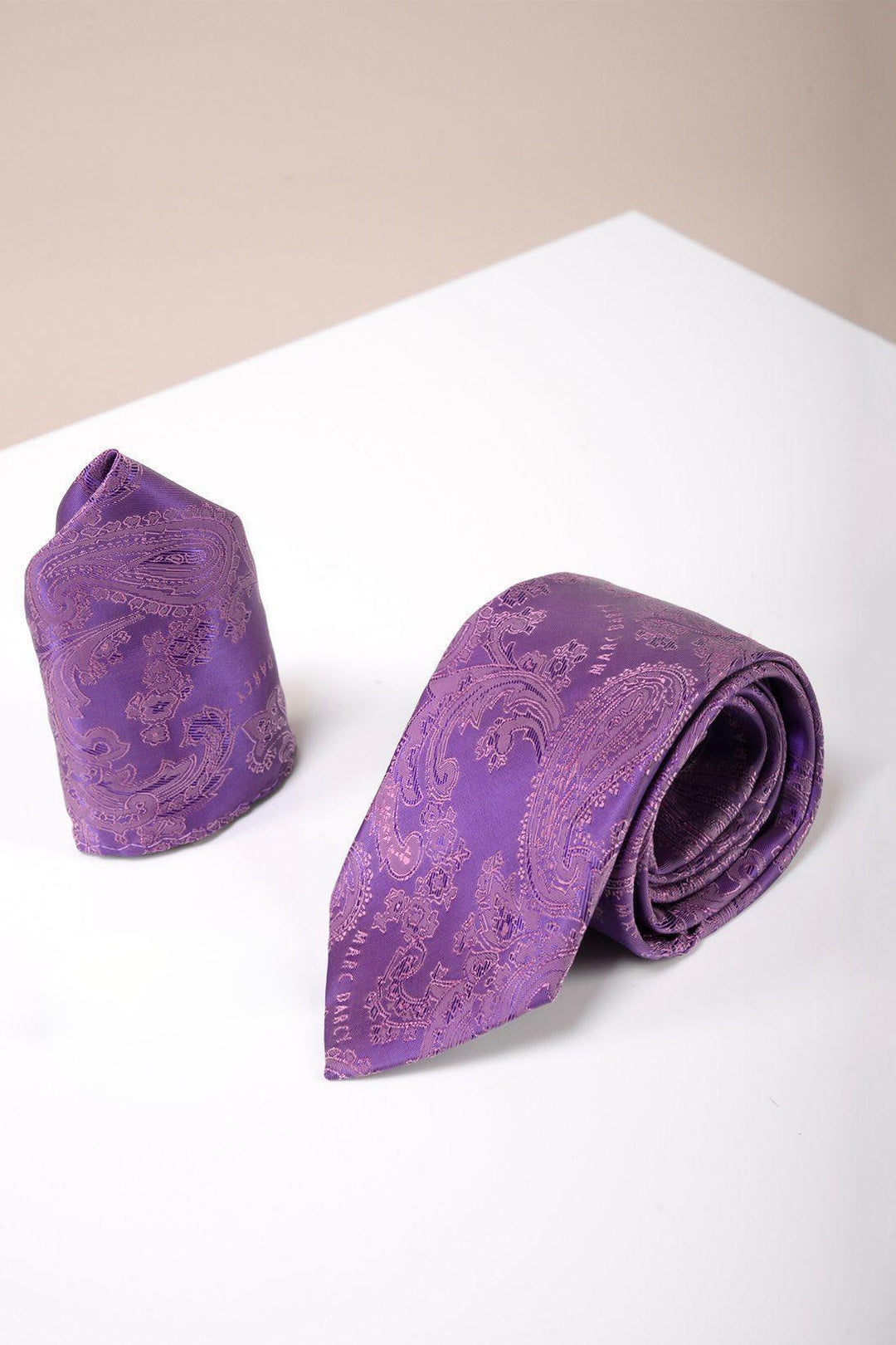 The Accessory PAISLEY - Purple Paisley Tie and Pocket Square Set is shown on a white surface with a beige background, making it an ideal choice for formal occasions.