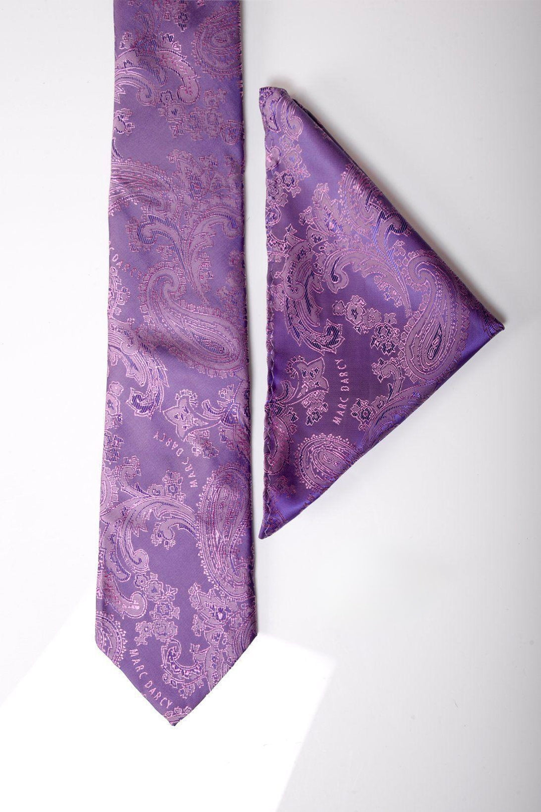The PAISLEY - Purple Paisley Tie and Pocket Square Set by Accessory features a deep purple paisley design, displayed on a white surface with the tie laid vertically and the pocket square folded diagonally beside it.