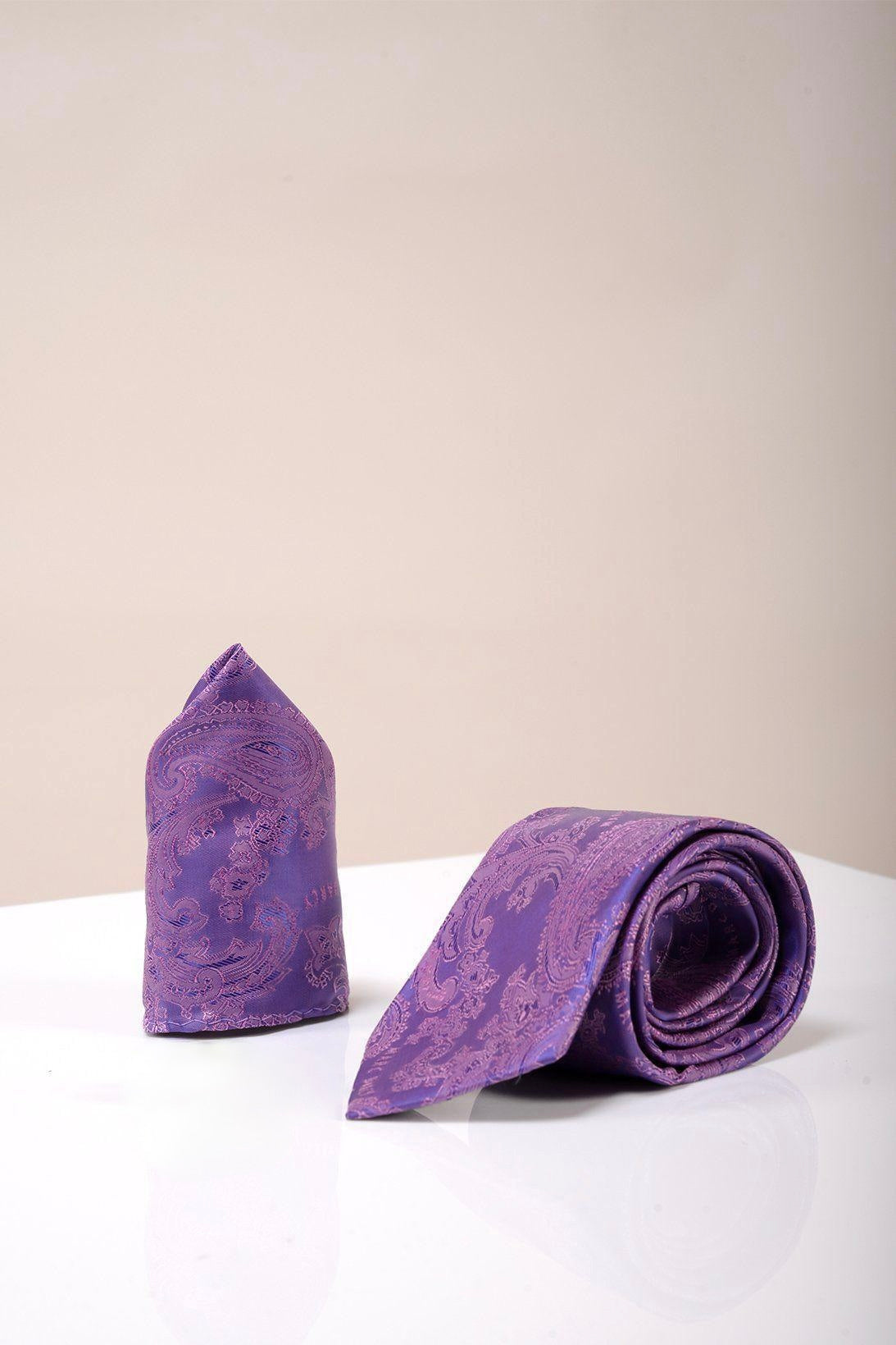 The Accessory PAISLEY Purple Paisley Tie and Pocket Square Set is elegantly rolled and folded on a glossy white surface, ideal for formal looks against a light beige background.