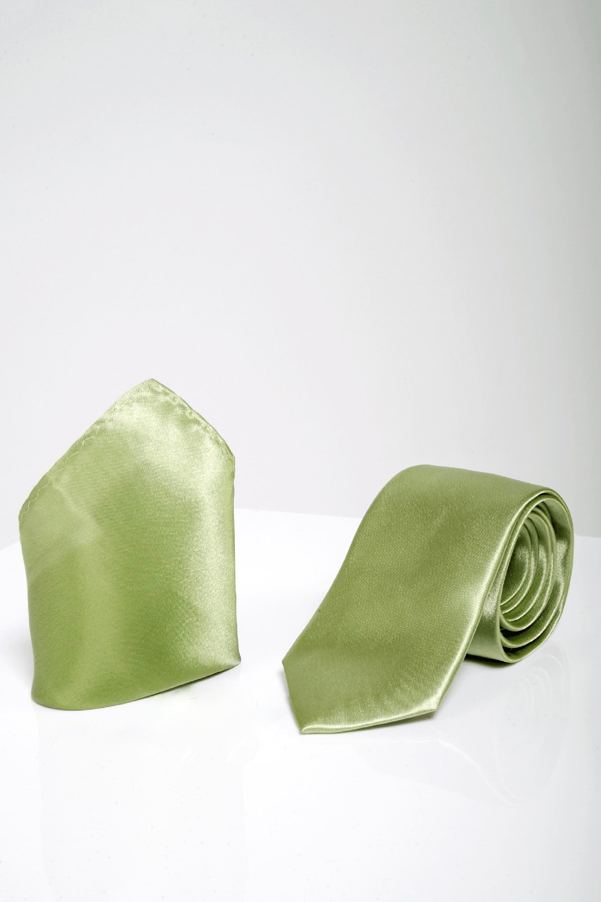 The ST - Satin Tie and Pocket Square Set In Green by Accessory features a light green satin tie and matching pocket square, elegantly rolled up on a white surface.
