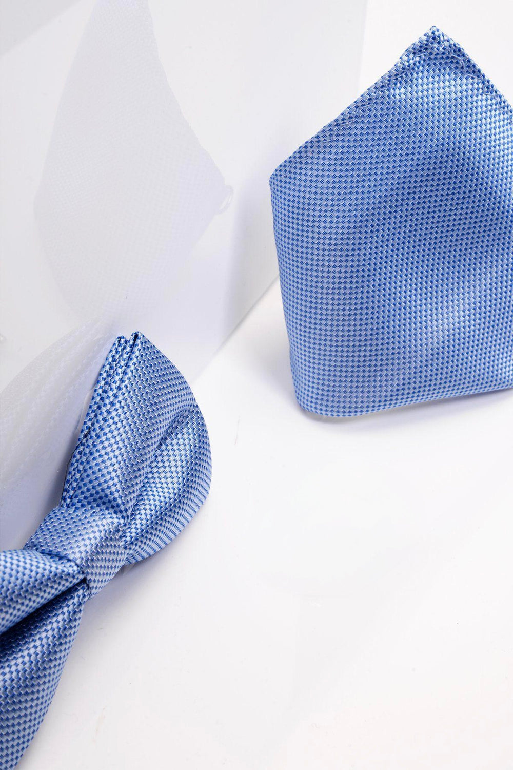 The Accessory TB17 Birdseye Print Bow Tie and Pocket Square Set in Blue is displayed on a white surface with soft shadows, presenting this pre-tied set as a refined wedding accessory.