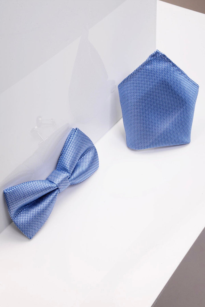 The Accessory TB17 Birdseye Print Bow Tie and Pocket Square Set in Blue, perfect for weddings, is displayed on a white surface with a clear divider reflecting both items.