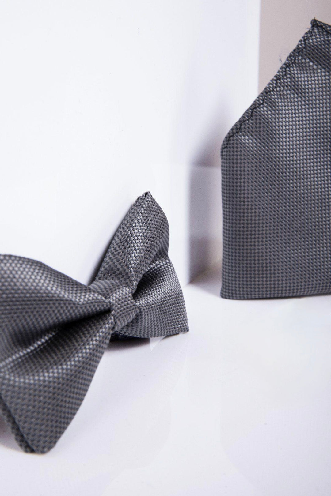 A close-up of the TB17 - Birdseye Print Bow Tie and Pocket Square Set in Charcoal by Accessory, featuring a stylish pre-tied design and textured finish, displayed against a white background.