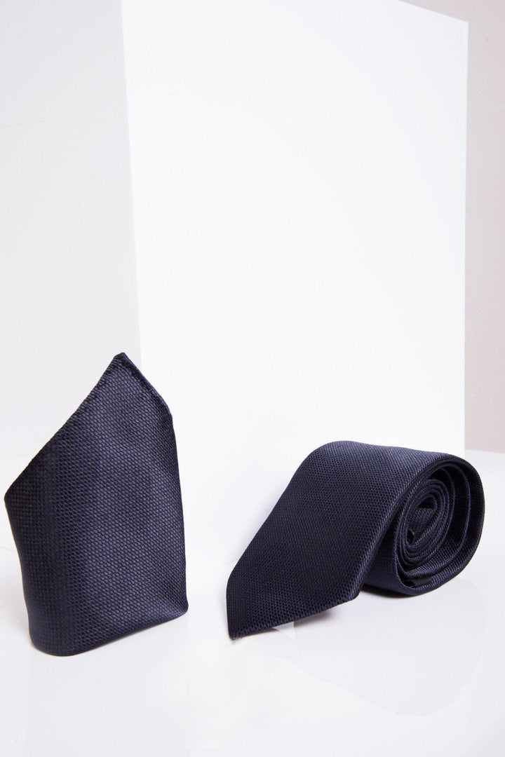 The Marc Darcy TB17 Birdseye Tie and Pocket Square Set in Midnight features a neatly folded pocket square and matching rolled tie, making an ideal wedding accessory—elegantly displayed against a white geometric backdrop.
