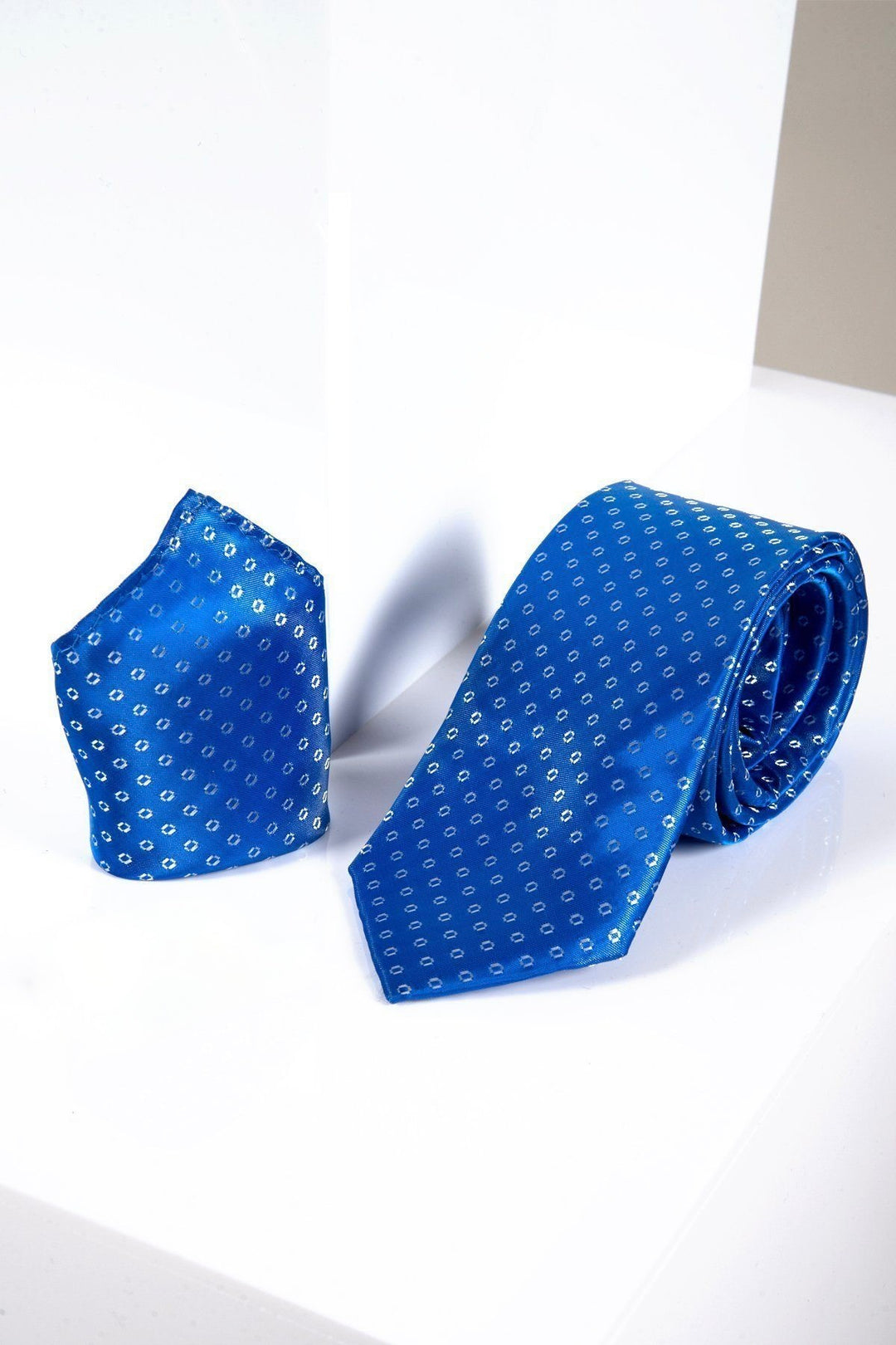 The Marc Darcy TS TUBES Blue Spot Tie and Pocket Square Set features small white geometric dots, displayed on a glossy white surface—perfect for formal occasions with elegant, monogrammed lining for a luxurious touch.