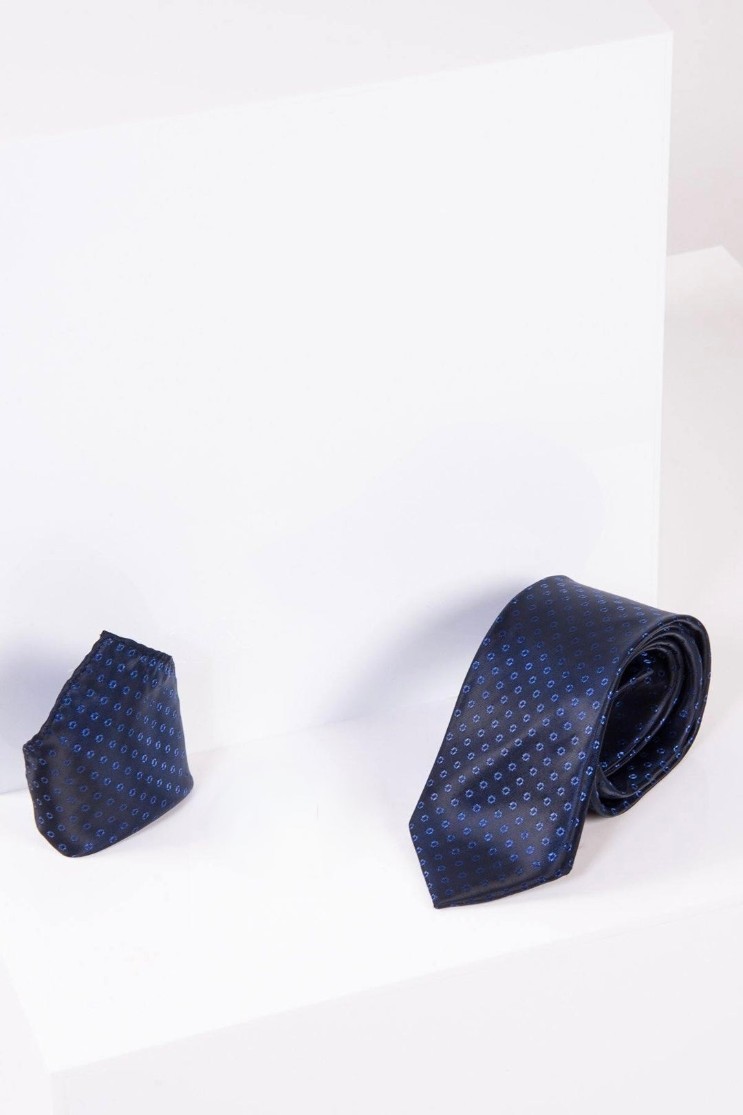 The Marc Darcy TS TUBES Navy Spot Tie and Pocket Square Set pairs a stylish navy dotted tie with a handmade pocket square, elegantly displayed on a white geometric background—ideal for luxury formal wear.