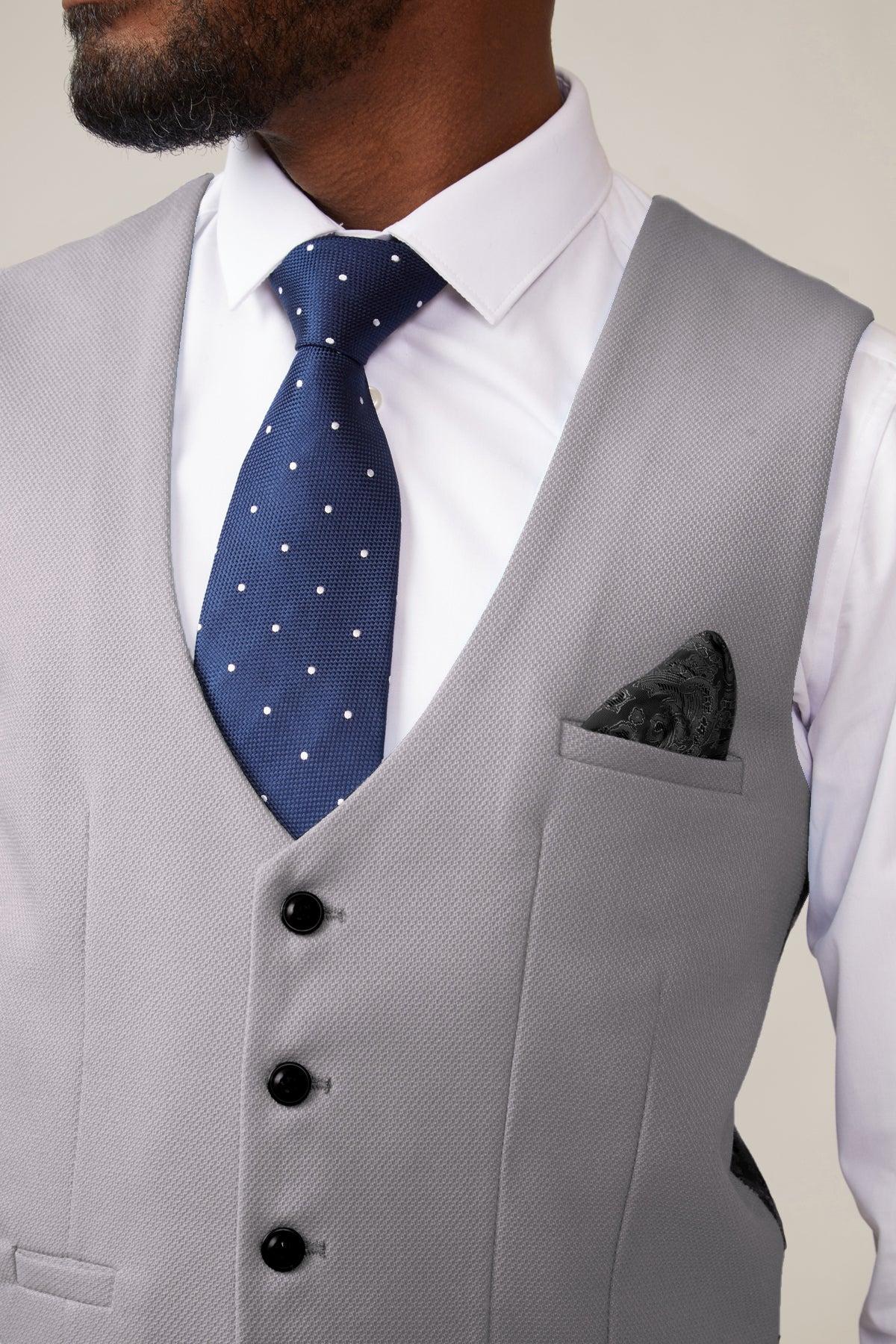 A man wears the marcdarcy KELVIN Silver Single Breasted Waistcoat over a white dress shirt, paired with a navy polka dot tie and dark patterned pocket square. Only his lower face, neck, and upper torso are visible.