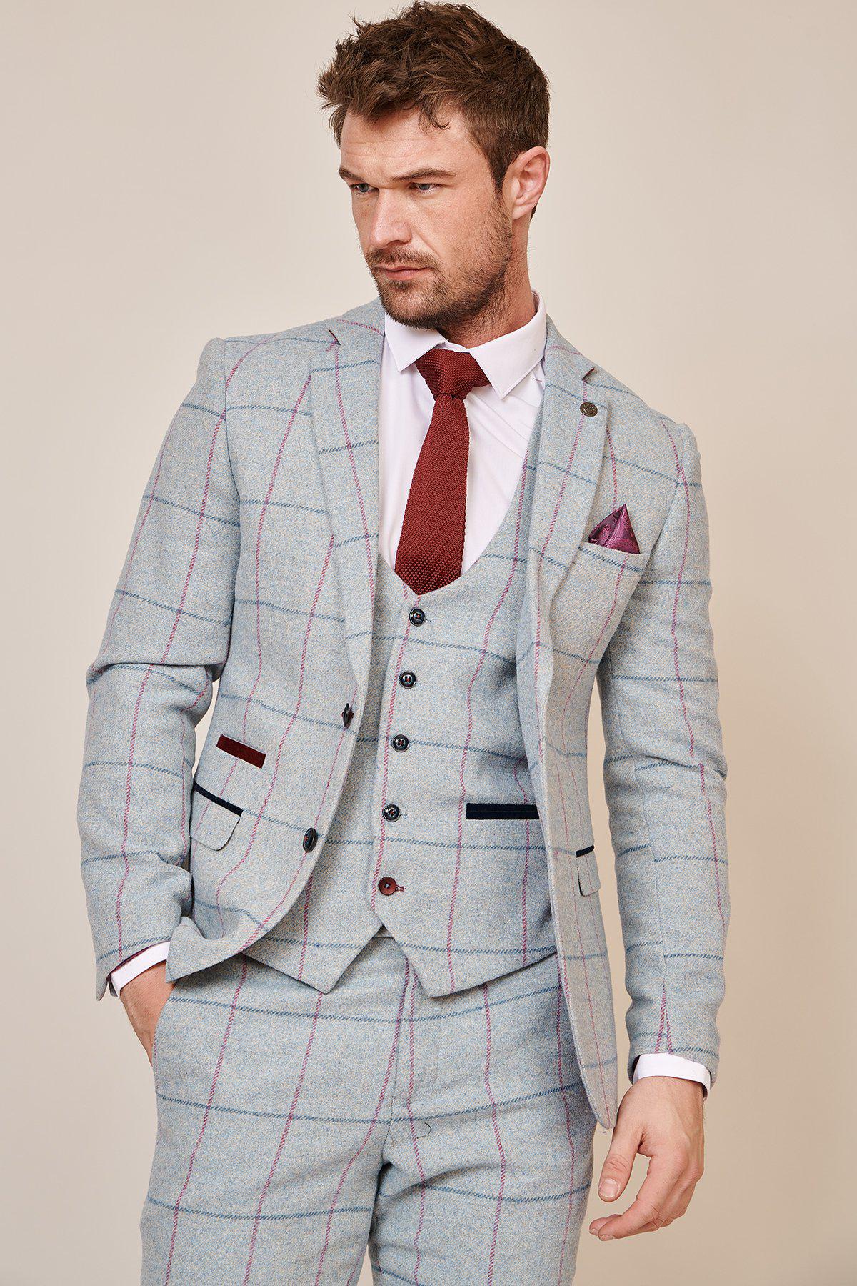 A man in the Marc Darcy NICOLAS Sky Check Tweed Blazer, styled with a white shirt, burgundy paisley tie, and matching pocket square, stands with hands in his pockets, gazing to the side.