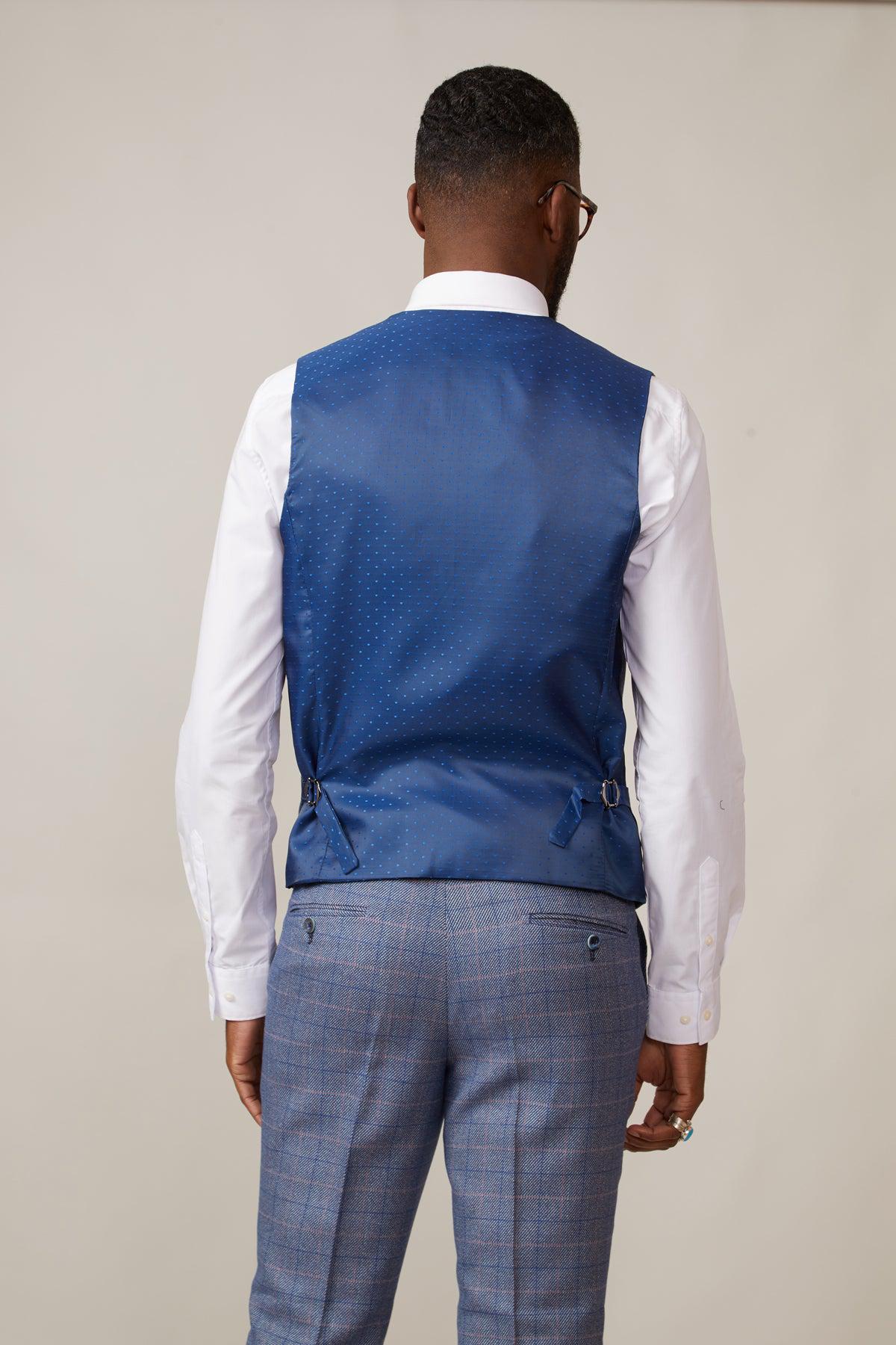A man with short hair, glasses, and a trimmed beard is seen from the back in vintage style, wearing the marcdarcy HILTON Blue Tweed Check Single Breasted Waistcoat over a white shirt and gray plaid trousers against a plain light background.