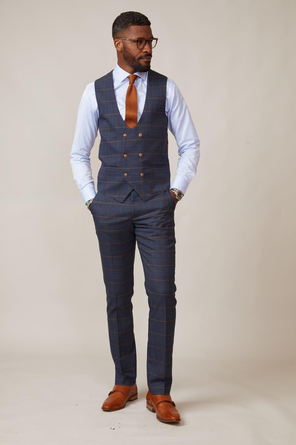 Boxing legend Frank Bruno wears the marcdarcy Jenson Marine Check Suit, paired with a light blue shirt, orange tie, glasses, and brown shoes.