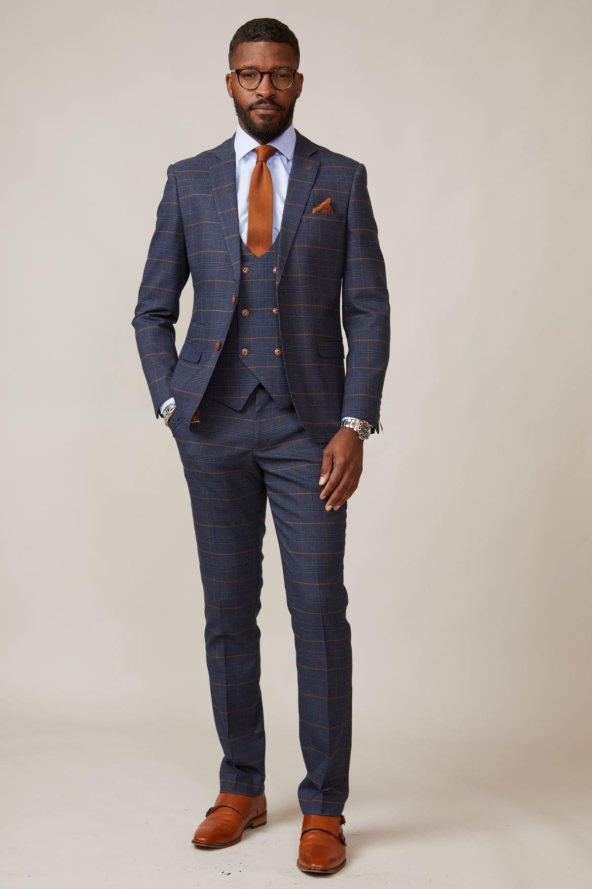 Actor Jamie Lomas poses in the marcdarcy Jenson Marine Check Suit, styled with brown shoes, a brown tie, and a brown pocket square against a plain light background.