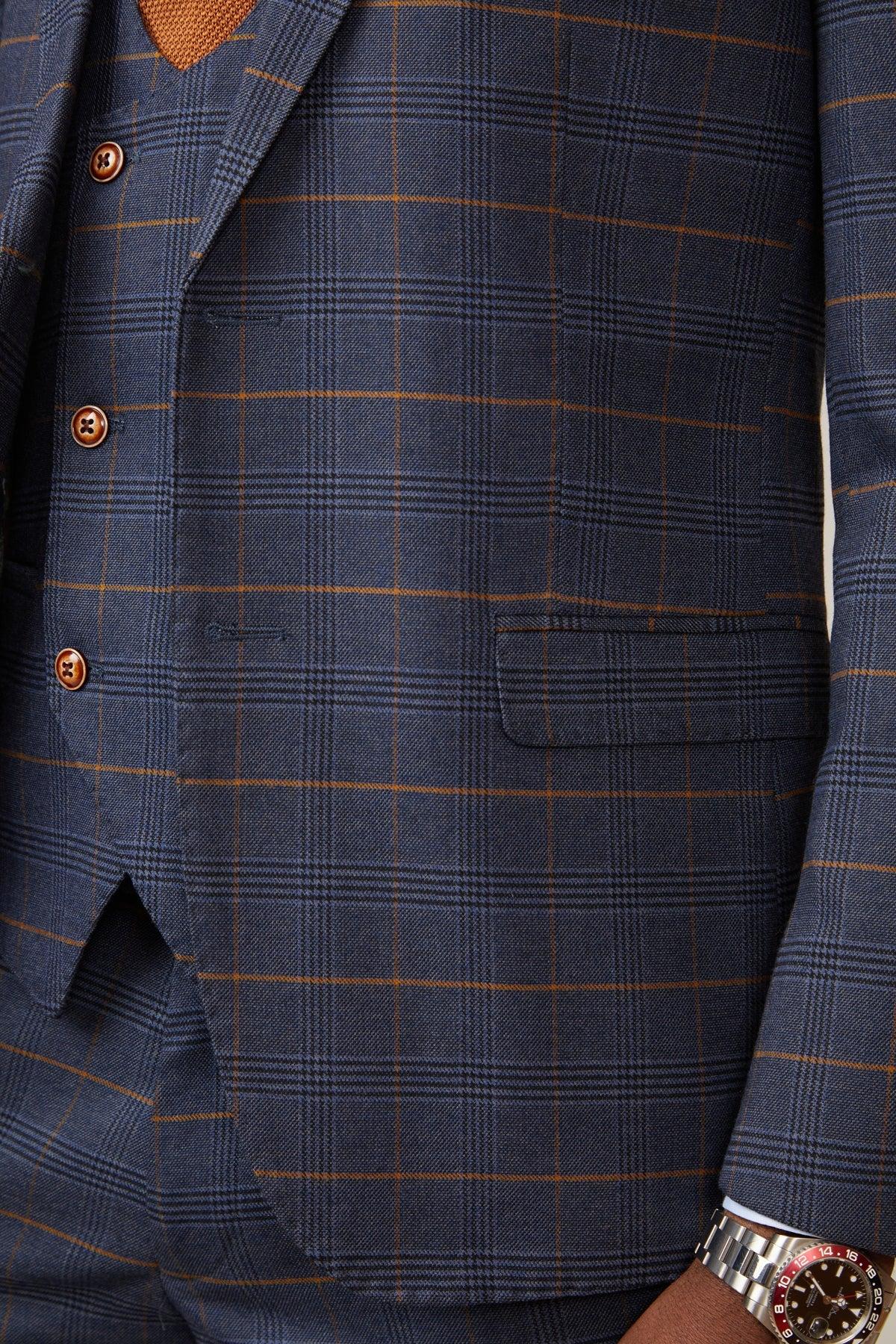 Close-up of Boxing Legend Frank Bruno in a marcdarcy Jenson Marine Check Suit. He wears a matching vest with three buttons, and an orange textured v-neck sweater shows beneath the three-piece suit.