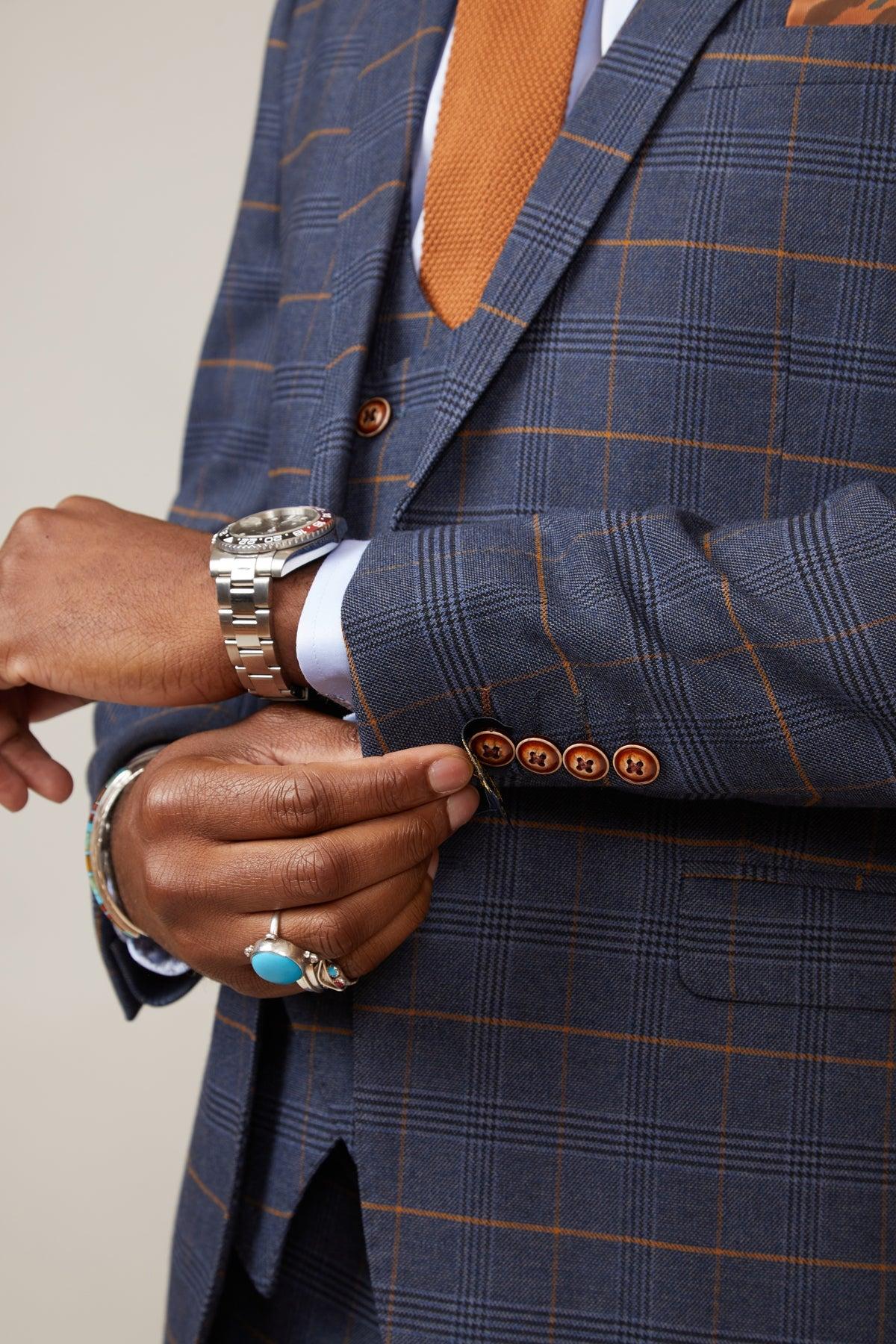 Boxing legend Frank Bruno adjusts the cuff of his marcdarcy Jenson Marine Check Suit, paired with an orange tie and a silver watch.