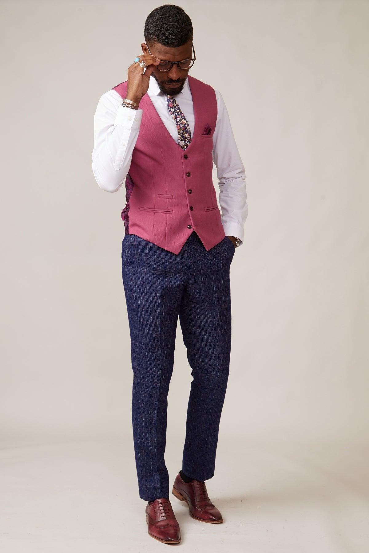 A man in the marcdarcy KELVIN - Berry Single Breasted Waistcoat, white shirt, floral tie, and plaid pants adjusts his glasses while looking down.
