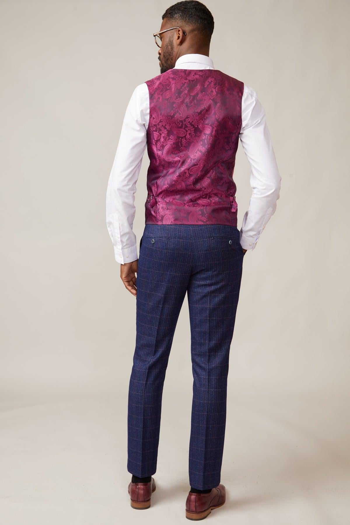 A man stands facing away in a white shirt, marcdarcy’s KELVIN - Berry Single Breasted Waistcoat, blue plaid trousers, and brown loafers—a stylish summer wedding look set against a simple, neutral background.