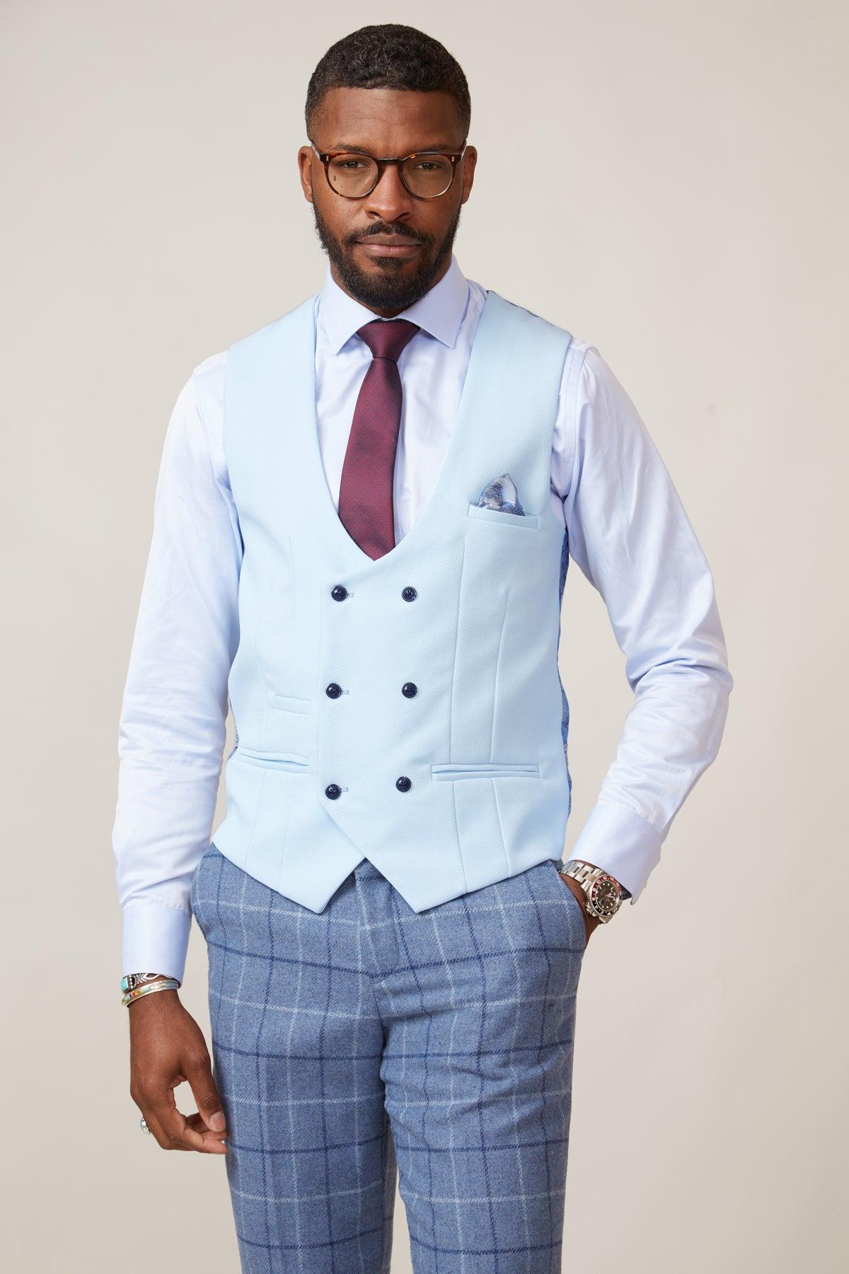 A man wearing glasses, the marcdarcy KELVIN Sky Blue Double Breasted Waistcoat over a white shirt with a burgundy tie and blue plaid trousers stands against a plain light background.