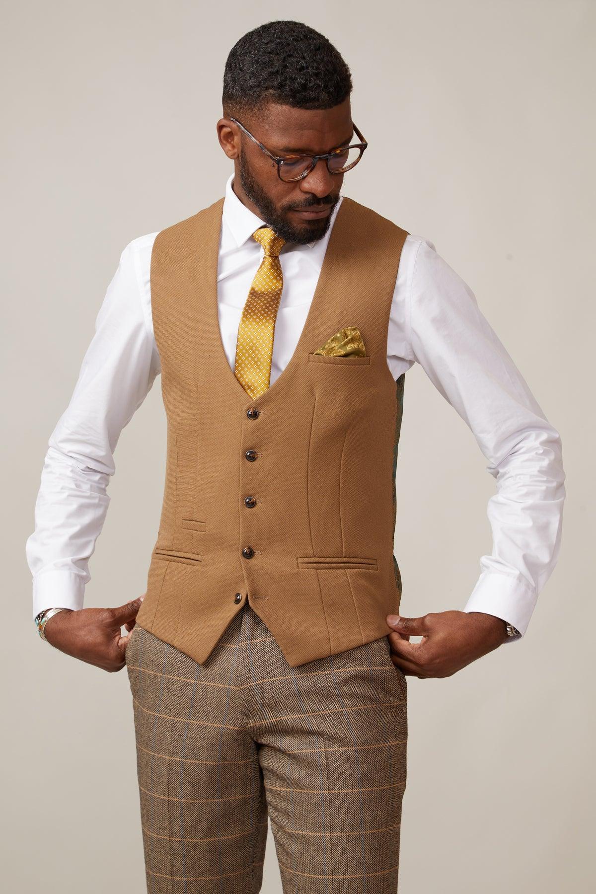 A man wearing glasses, a white dress shirt, a mustard yellow tie, plaid brown trousers, and the marcdarcy KELVIN - Oak Single Breasted Waistcoat looks down while adjusting his slim fit vest.