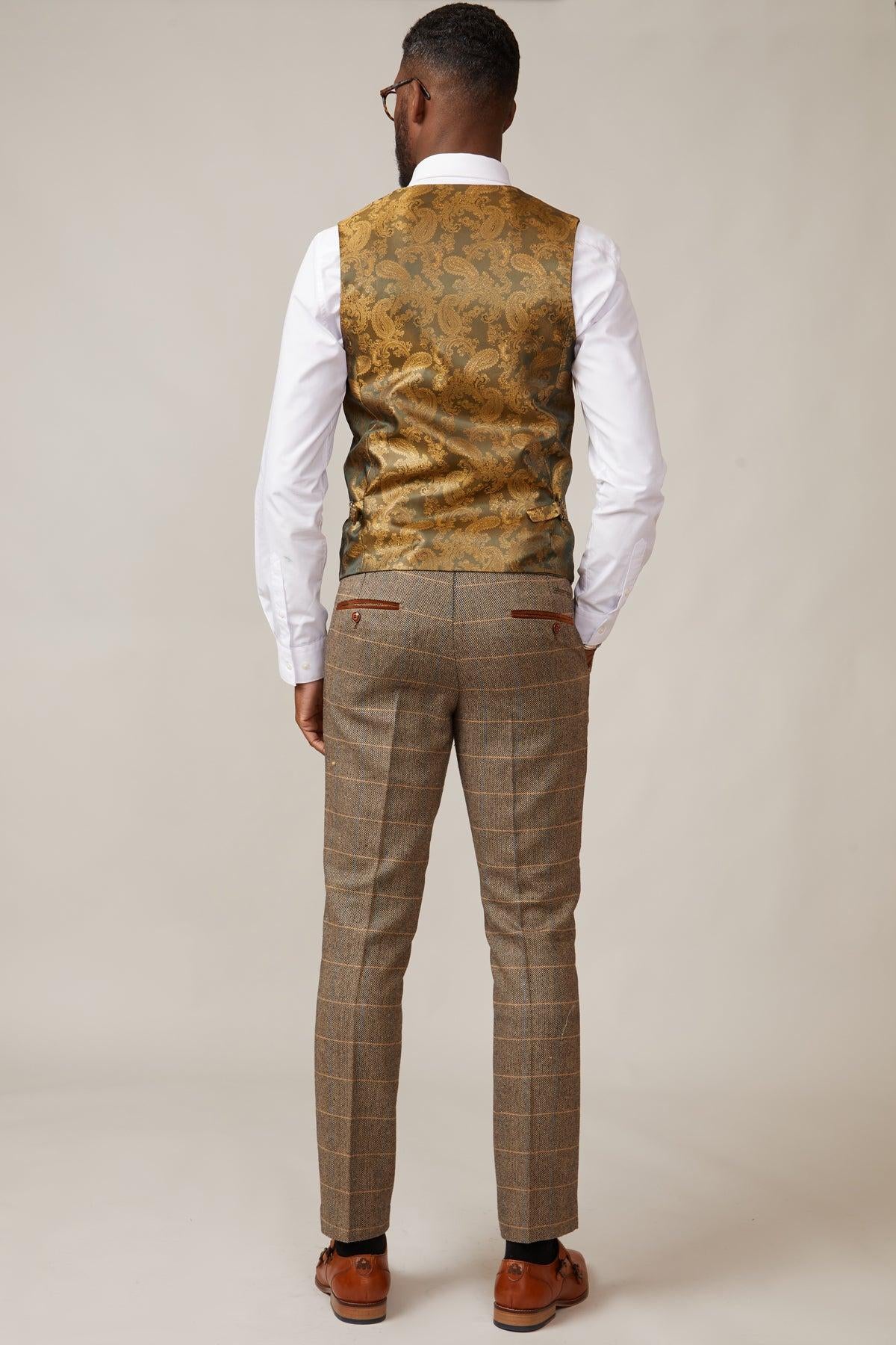 A man faces away, wearing the marcdarcy KELVIN Tan Single Breasted Waistcoat over a white shirt, paired with brown plaid trousers and brown dress shoes, set against a plain light background.