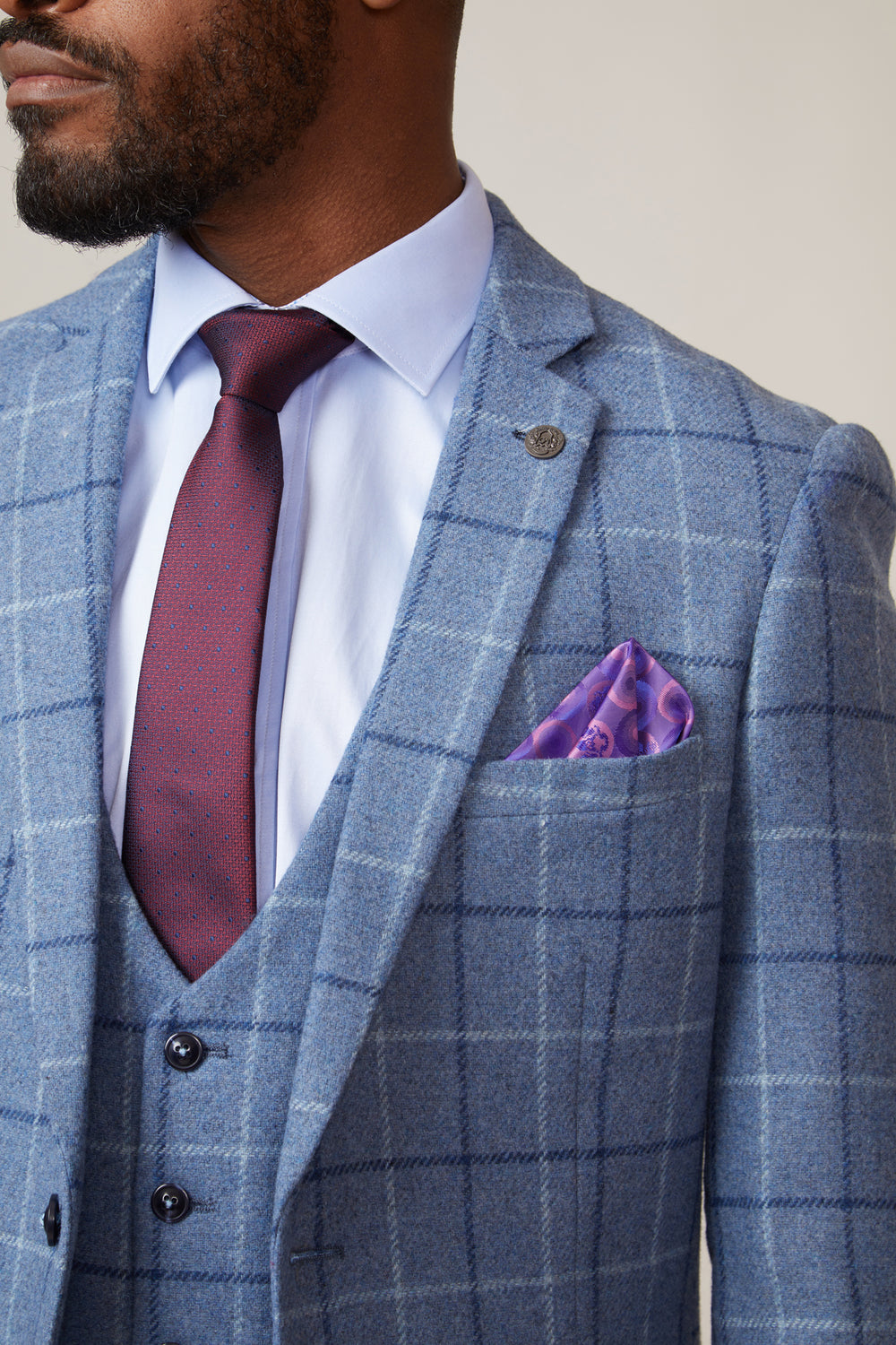A man wears the marcdarcy CLINTON - Blue Tweed Check Blazer with a matching vest, light blue shirt, burgundy tie, and a purple patterned pocket square. The image showcases the blazer’s details from shoulders to chest.