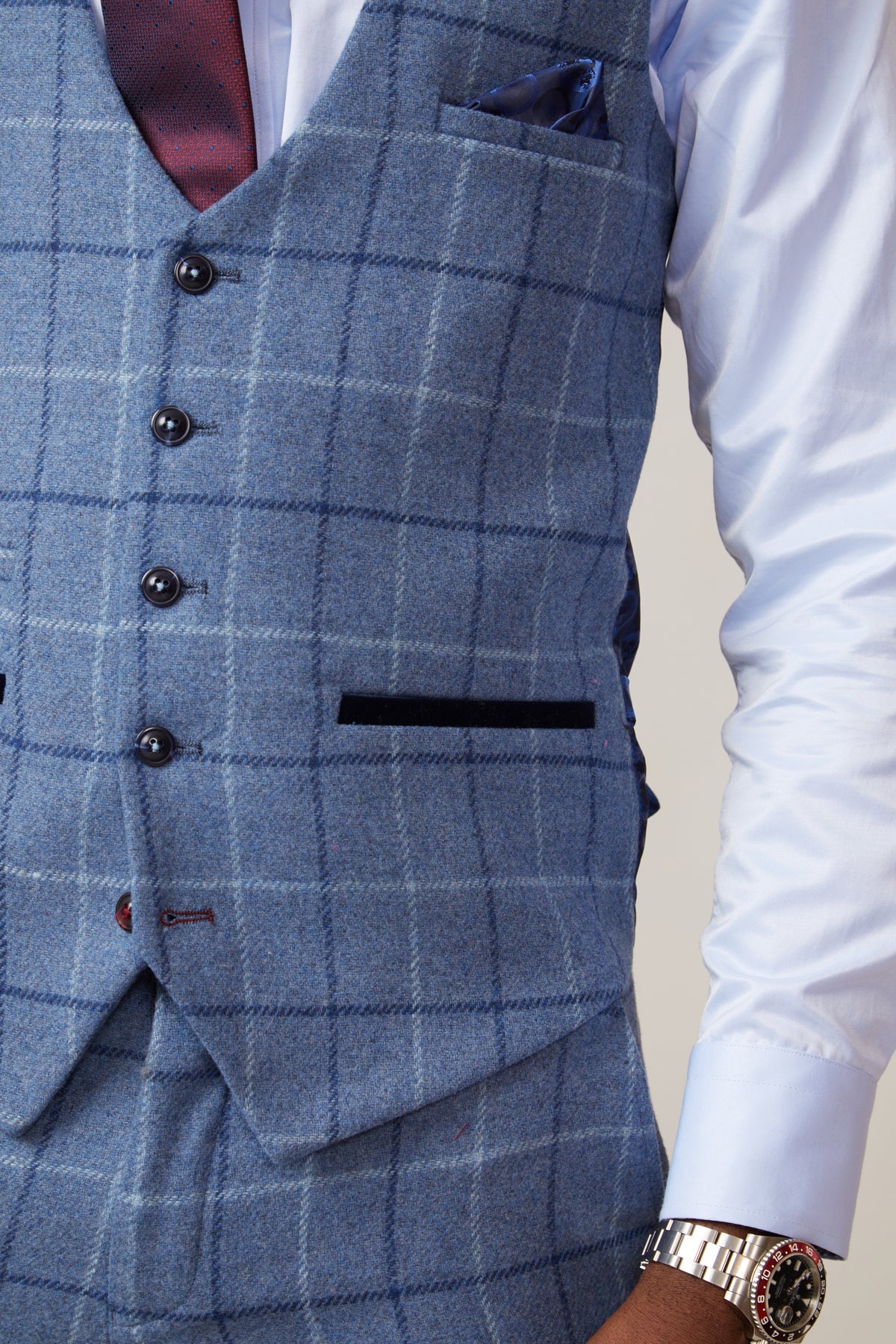 A person wearing the marcdarcy CLINTON Blue Tweed Check Waistcoat with matching trousers, a white shirt, dark red tie, blue pocket square, and silver wristwatch; only the torso and part of one arm are visible.