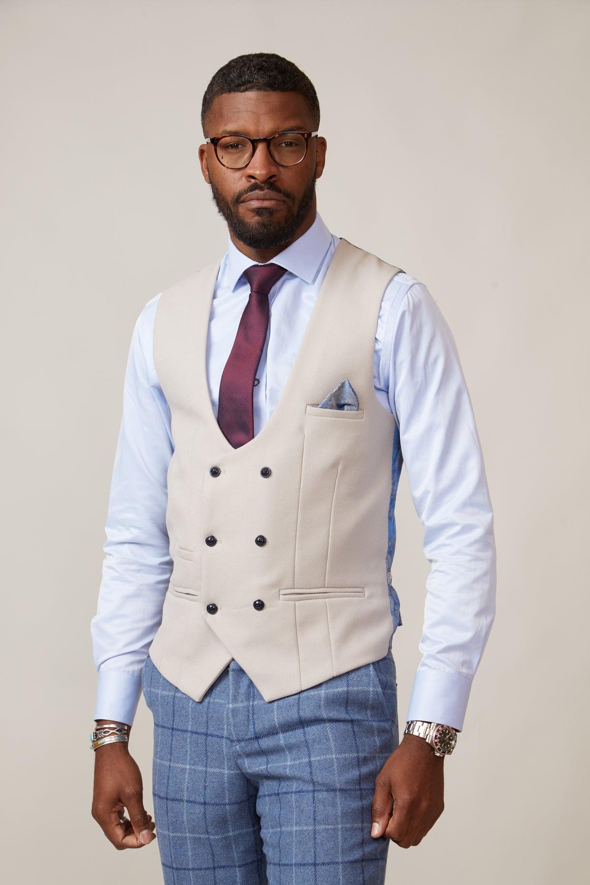 A man in glasses, a light blue shirt, red tie, marcdarcy KELVIN Stone Double Breasted Waistcoat, and slim fit blue plaid trousers stands against a plain light background, accessorized with a pocket square, watch, and bracelets.