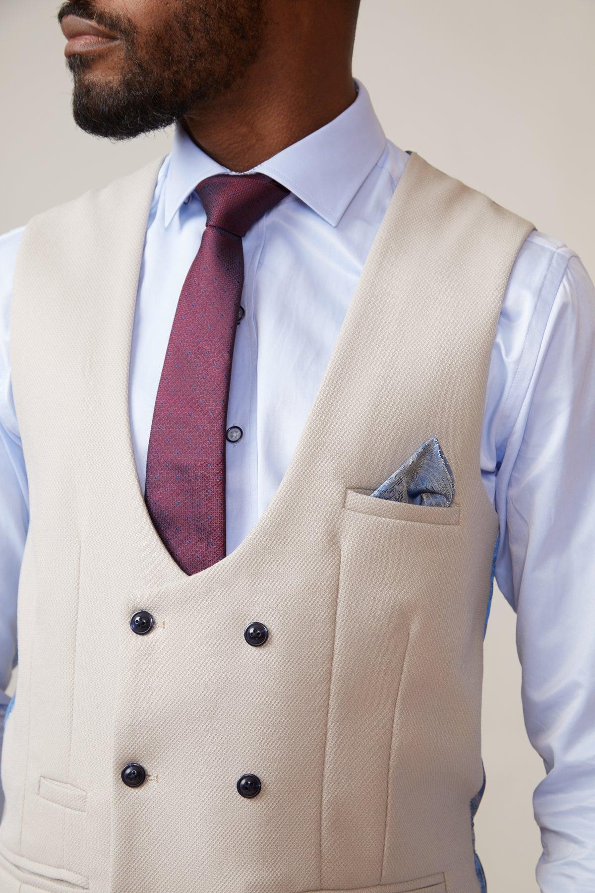 A man wears the marcdarcy KELVIN - Stone Double Breasted Waistcoat in slim fit over a light blue dress shirt, paired with a maroon tie and blue pocket square. His head is turned to the side, partially obscuring his face.